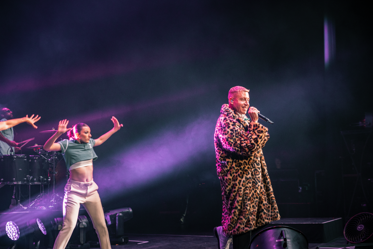 Energetic performers on stage with purple lighting effects during a dynamic concert performance.
