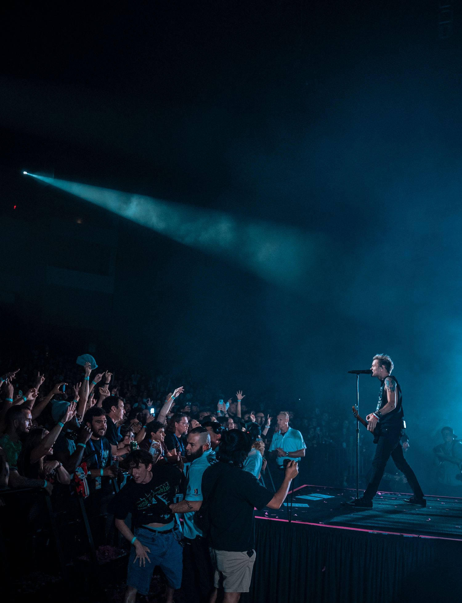 Concert audience with raised hands enjoying live performance under moody blue stage lights.