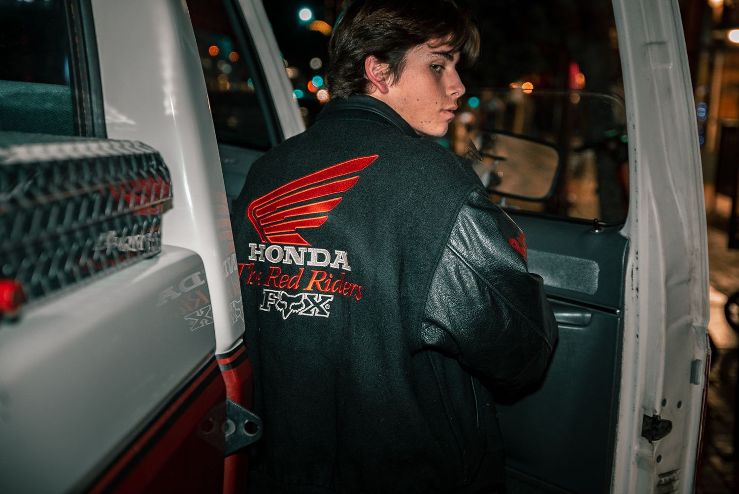 Person wearing Honda racing jacket seen from behind entering vehicle.