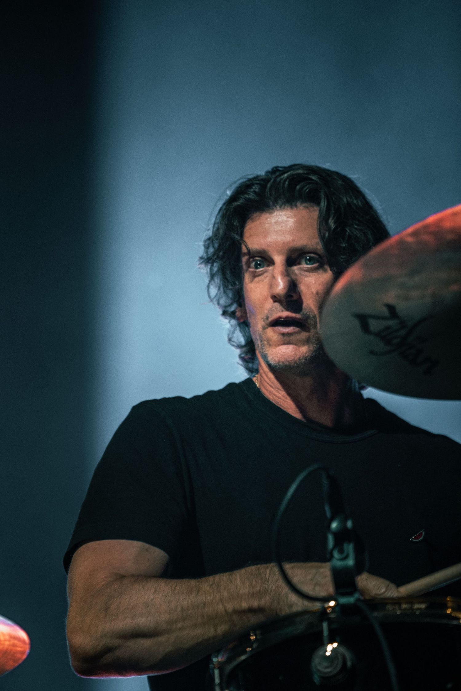 Close-up shot of drummer performing behind drum kit with dramatic side lighting.