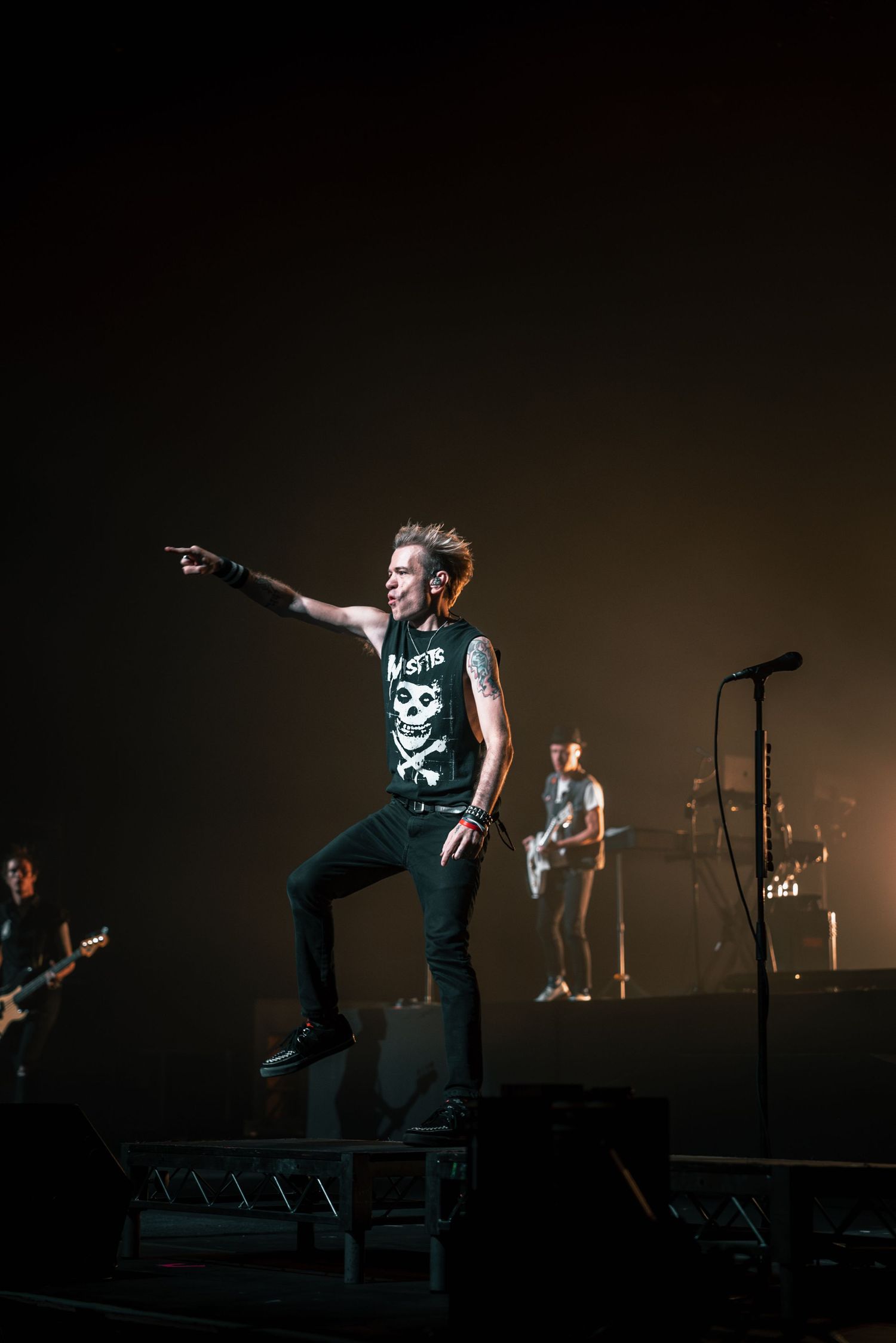 Rock performer in black outfit jumping on stage during concert performance.