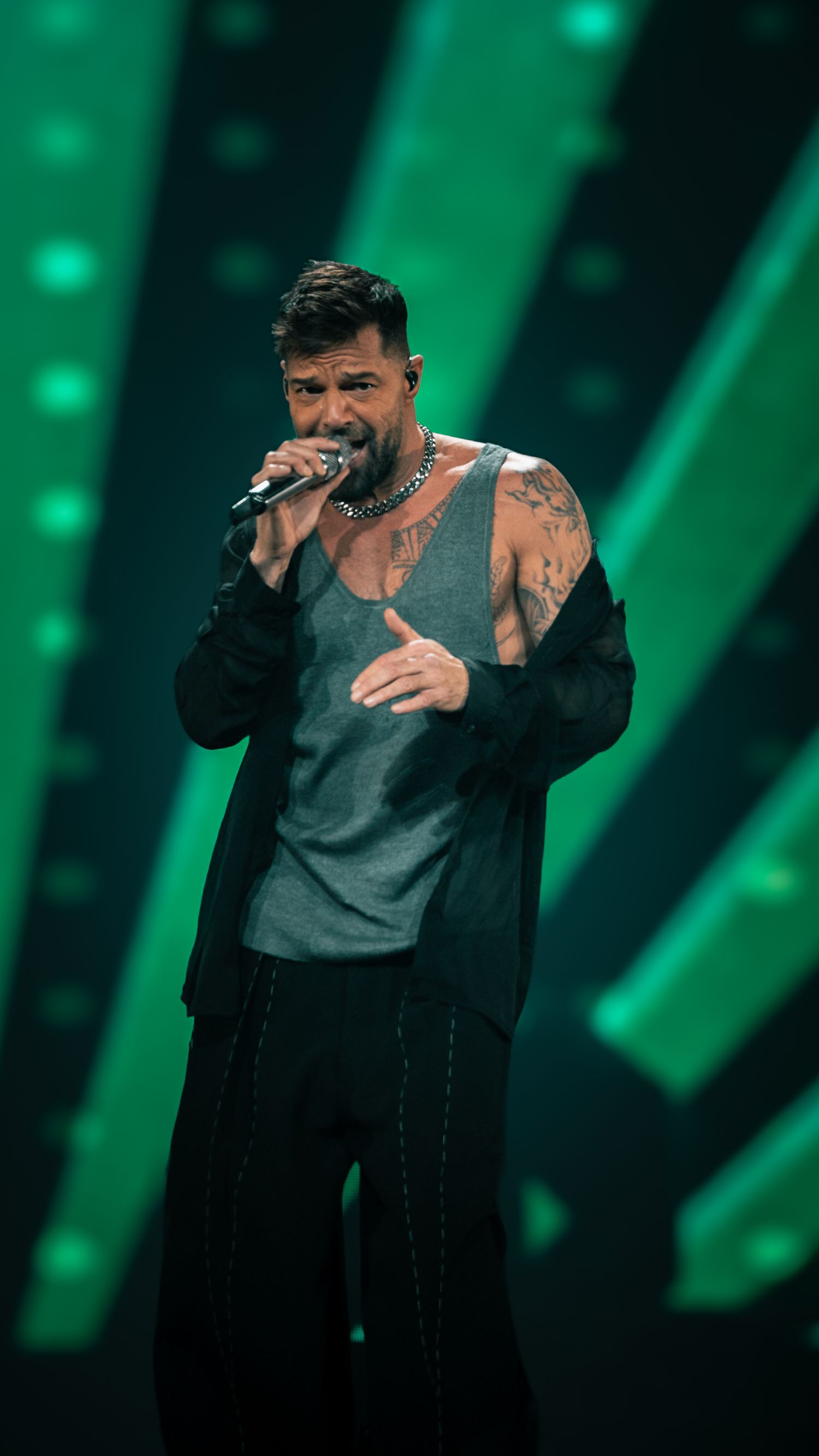 Singer performing in gray shirt and black jacket against green stage lighting.