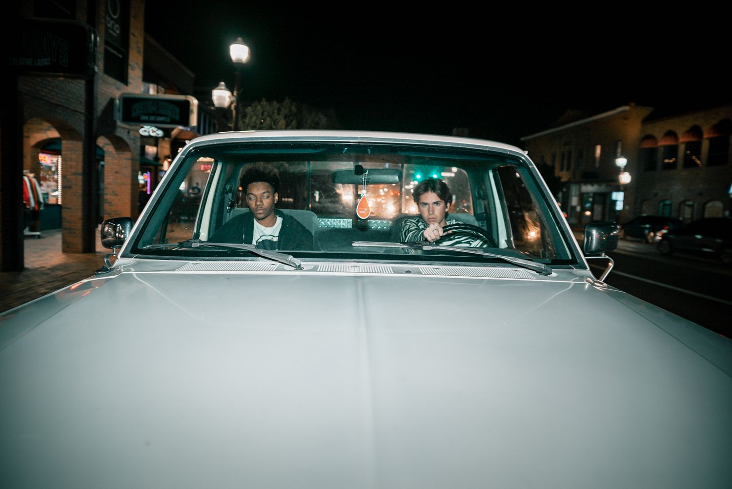 Night street scene showing occupants inside vintage car with urban lighting.