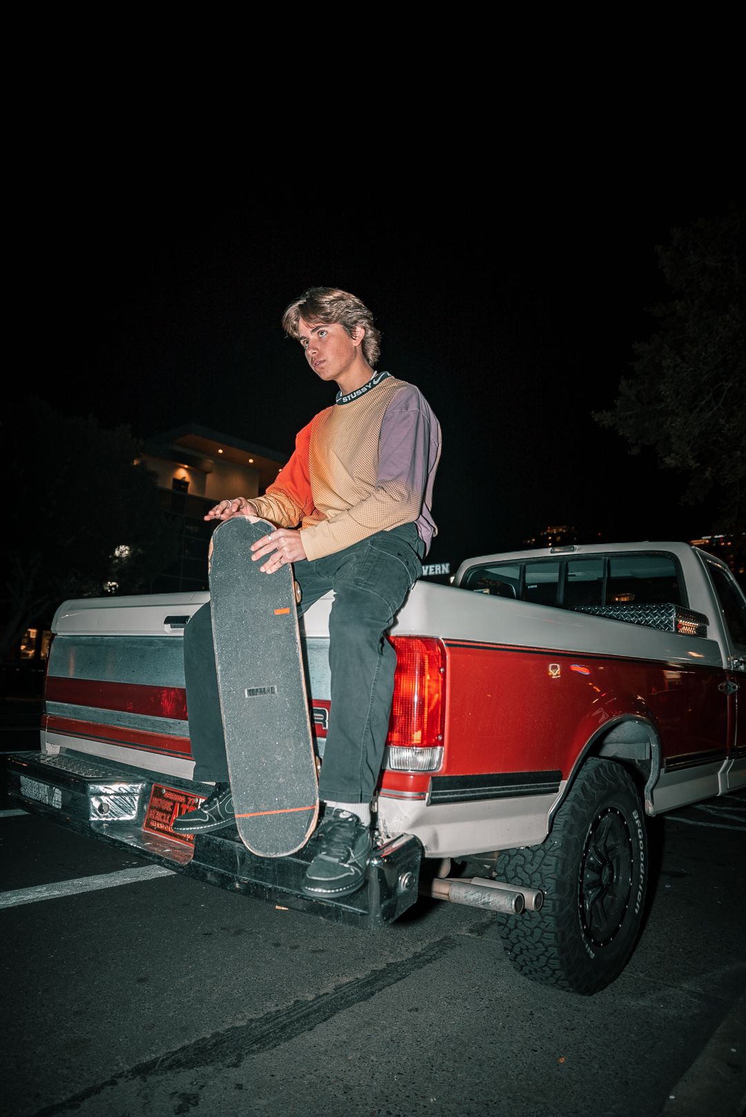 People sitting on the back of a red and white pickup truck at night.