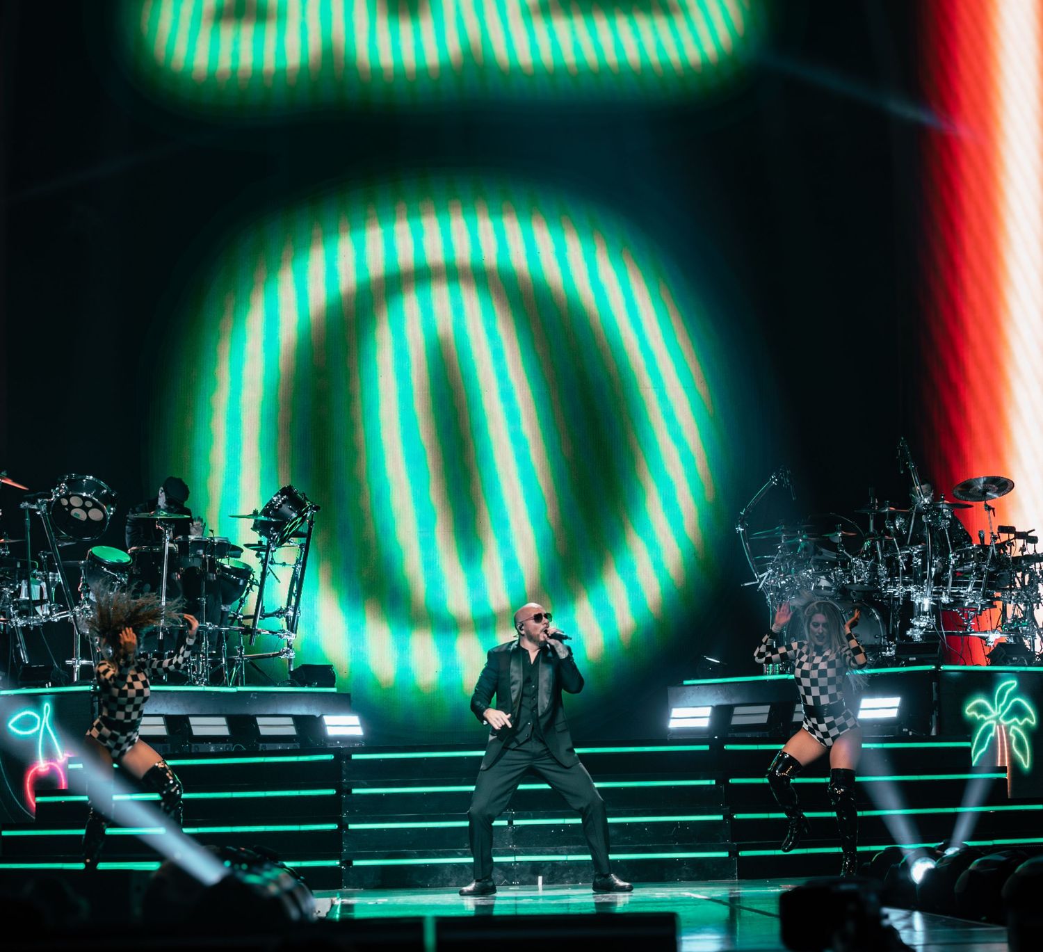 Concert performance with large green neon circle backdrop and tiered stage setup.