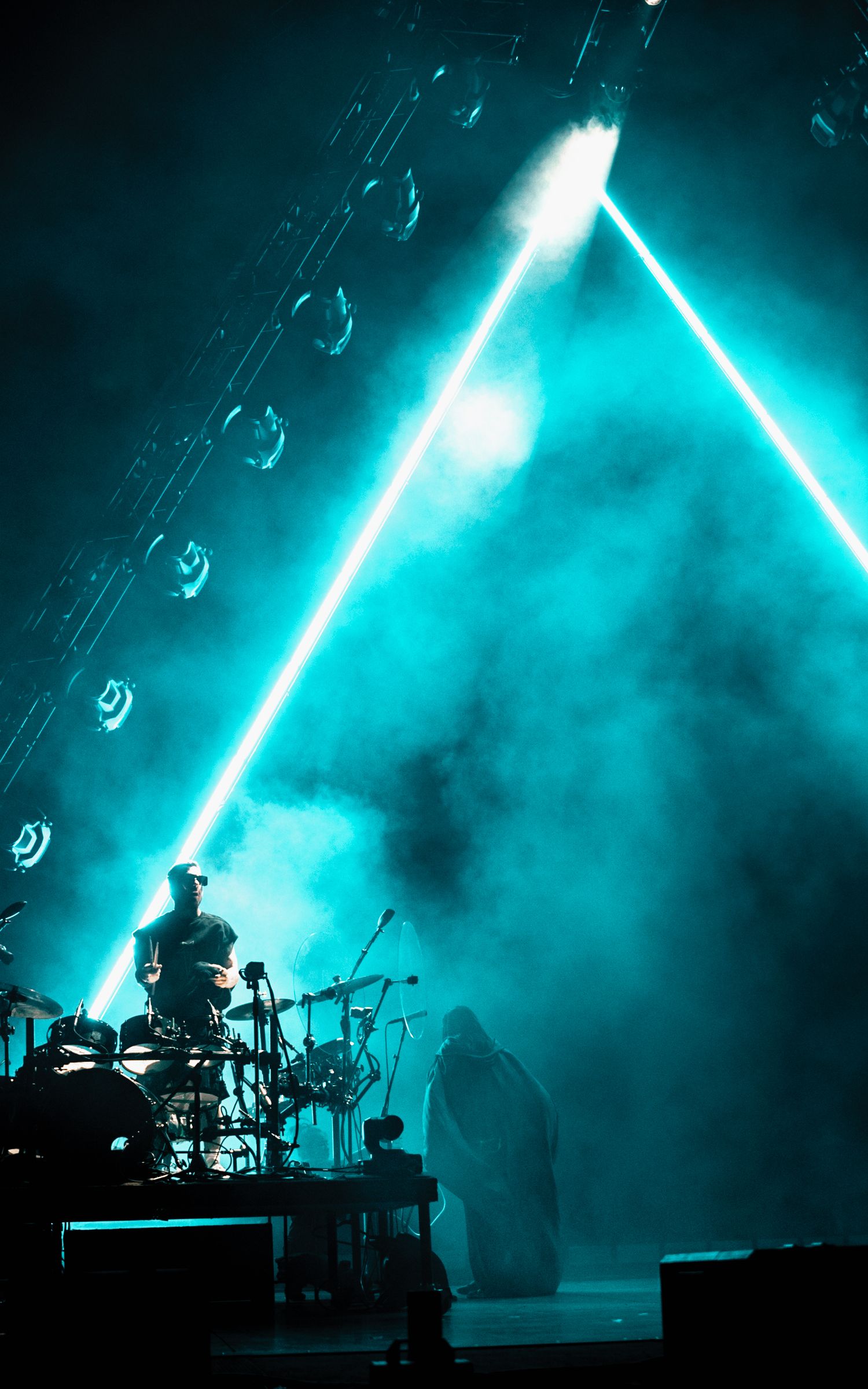 A concert stage bathed in ethereal blue lighting with a geometric triangle design.
