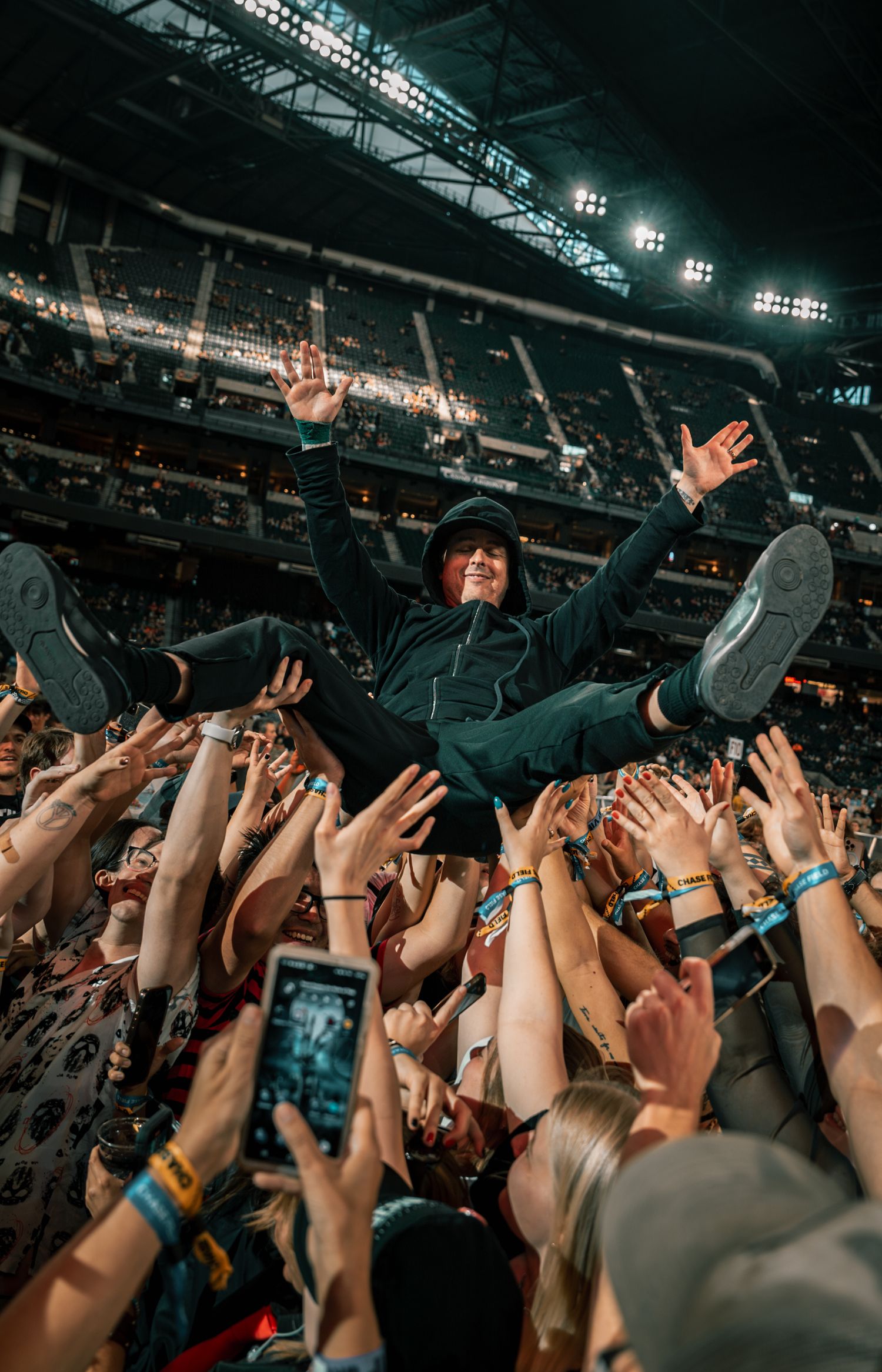 Performer crowd surfs on hands of concert audience while fans take photos on phones.
