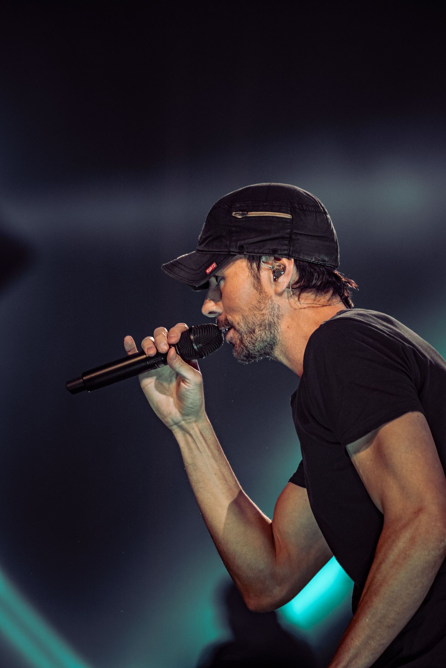 Close-up of performer in black hat singing passionately into microphone with blue lighting.