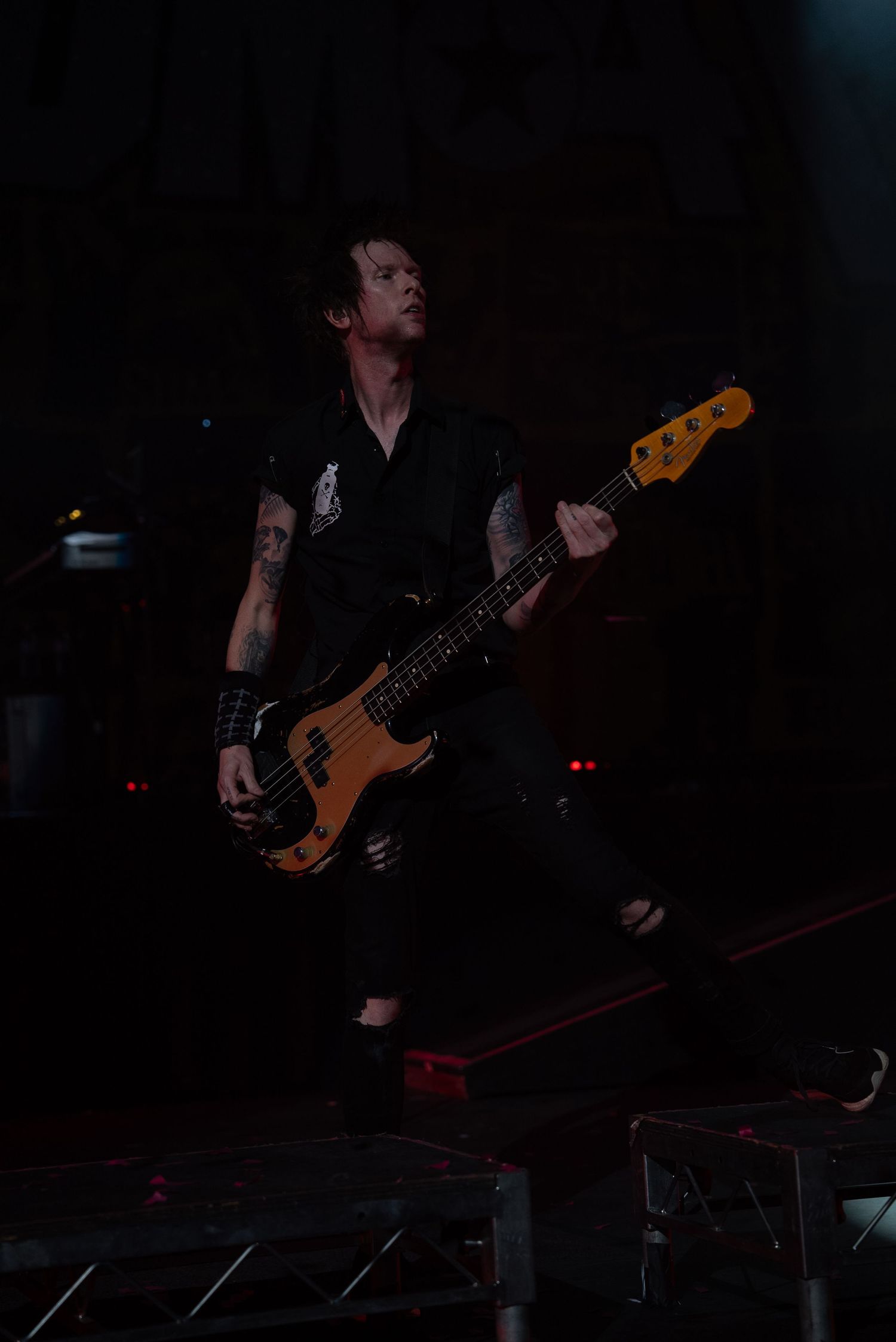 Bass guitarist performs dramatic jump while playing on dark concert stage.
