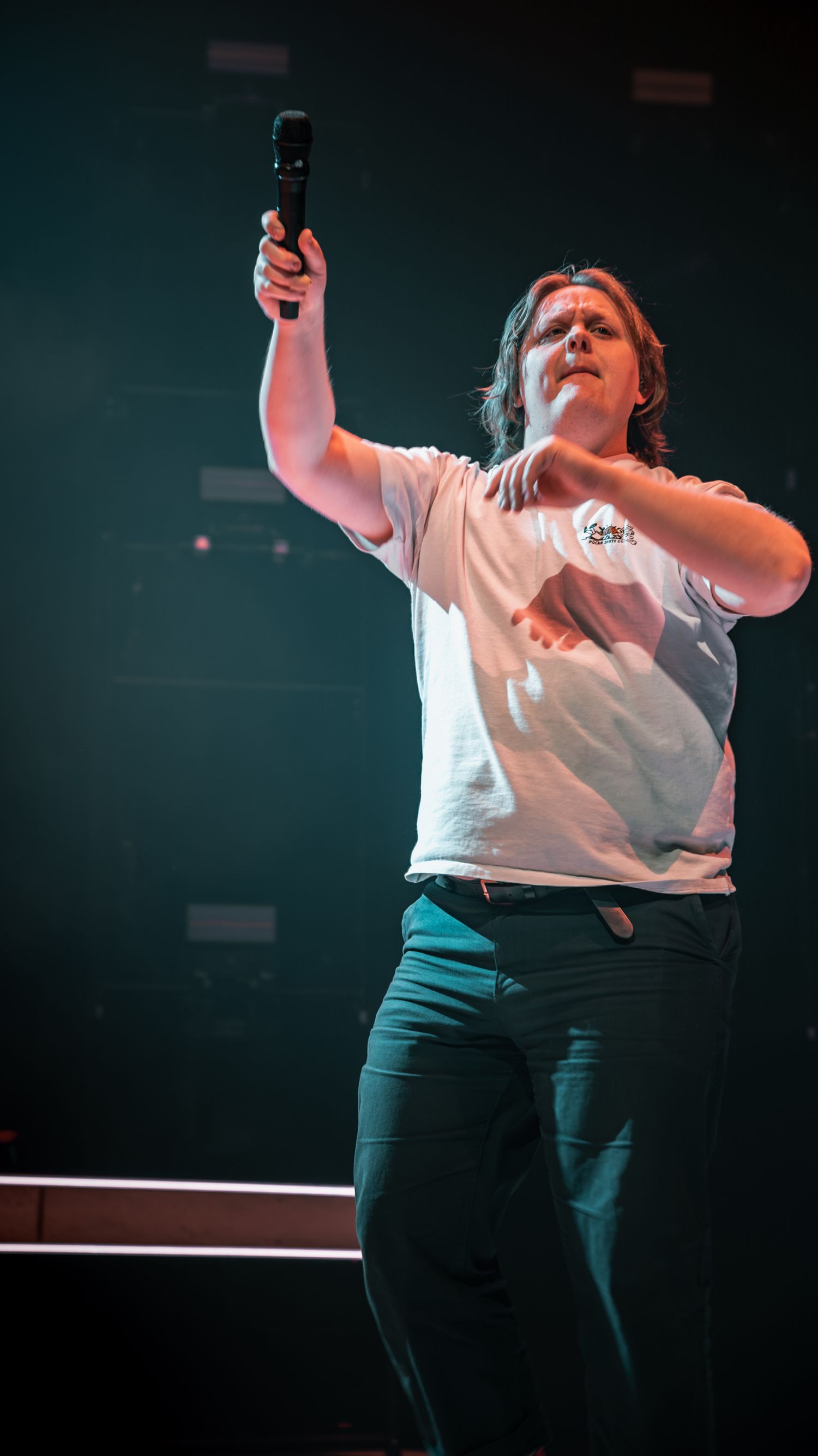 Stage performer in white shirt and dark pants singing emotionally during live performance.
