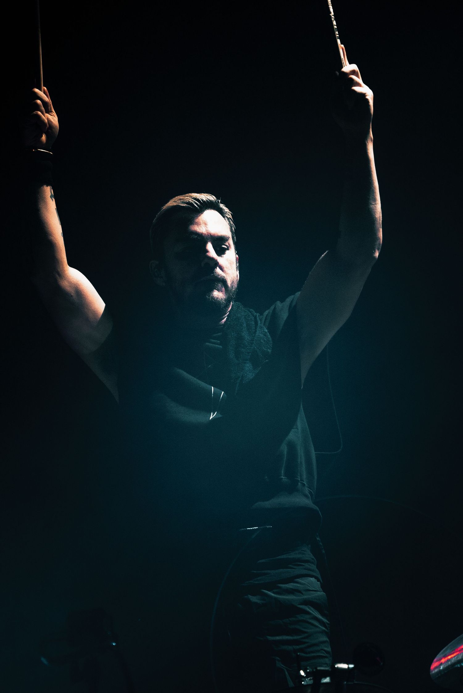 A performer raises their arms dramatically on stage in dramatic lighting.