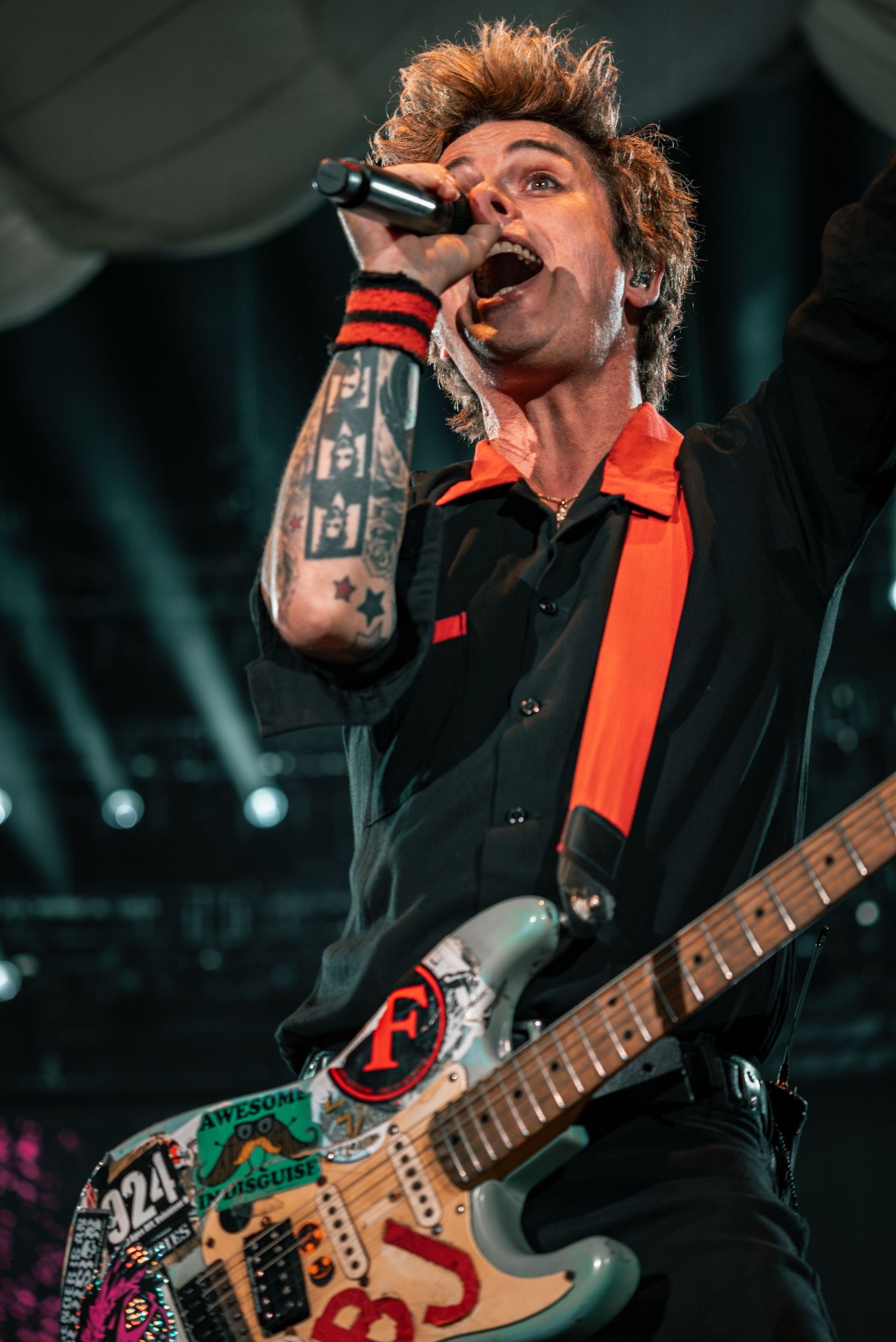 Close-up performance shot showing decorated electric guitar and dramatic stage lighting.