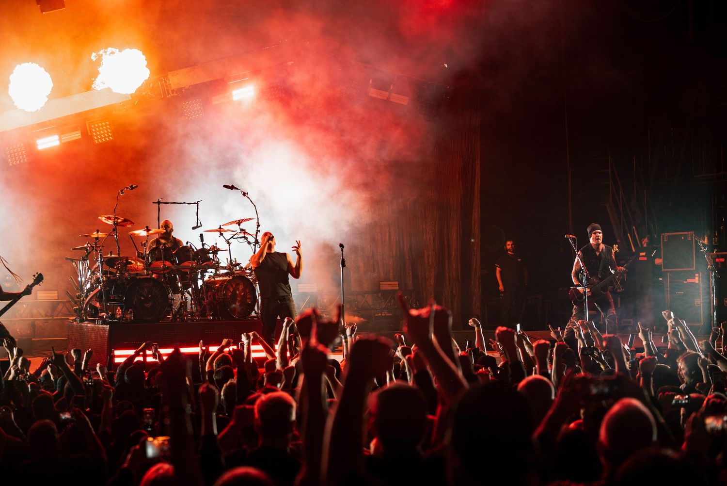 Concert crowd silhouetted against bright orange stage lighting and smoke effects.