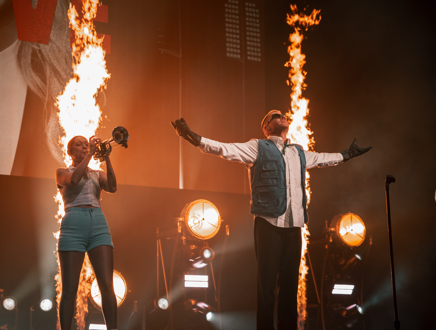 Dynamic concert performance with pyrotechnic flame effects and performers on stage.