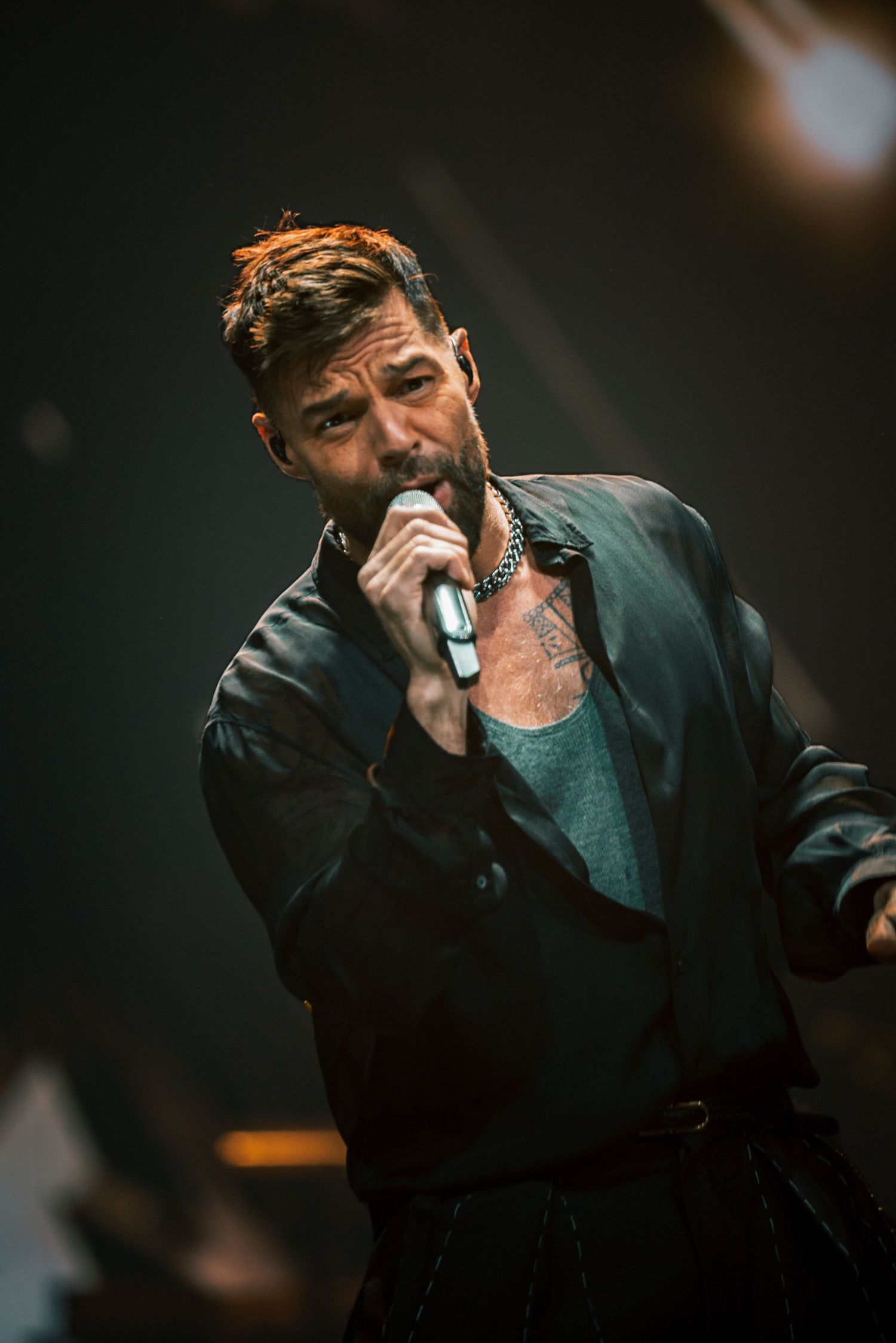 Artist in dark clothing singing emotionally into microphone during stage performance.