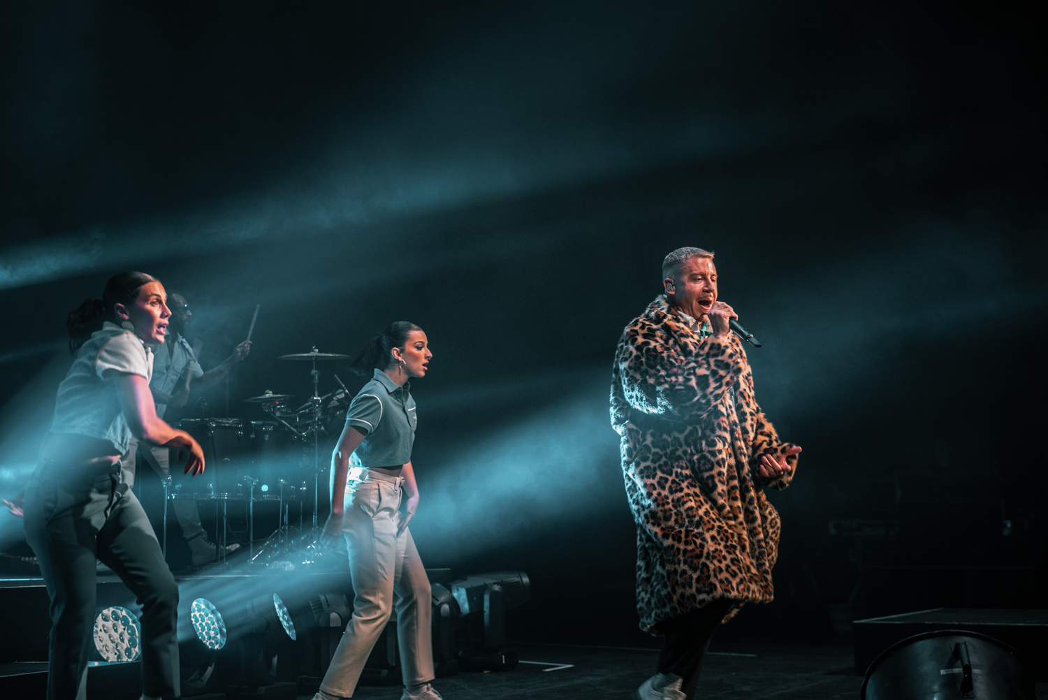Performers in contrasting outfits dance on stage under moody blue lighting.
