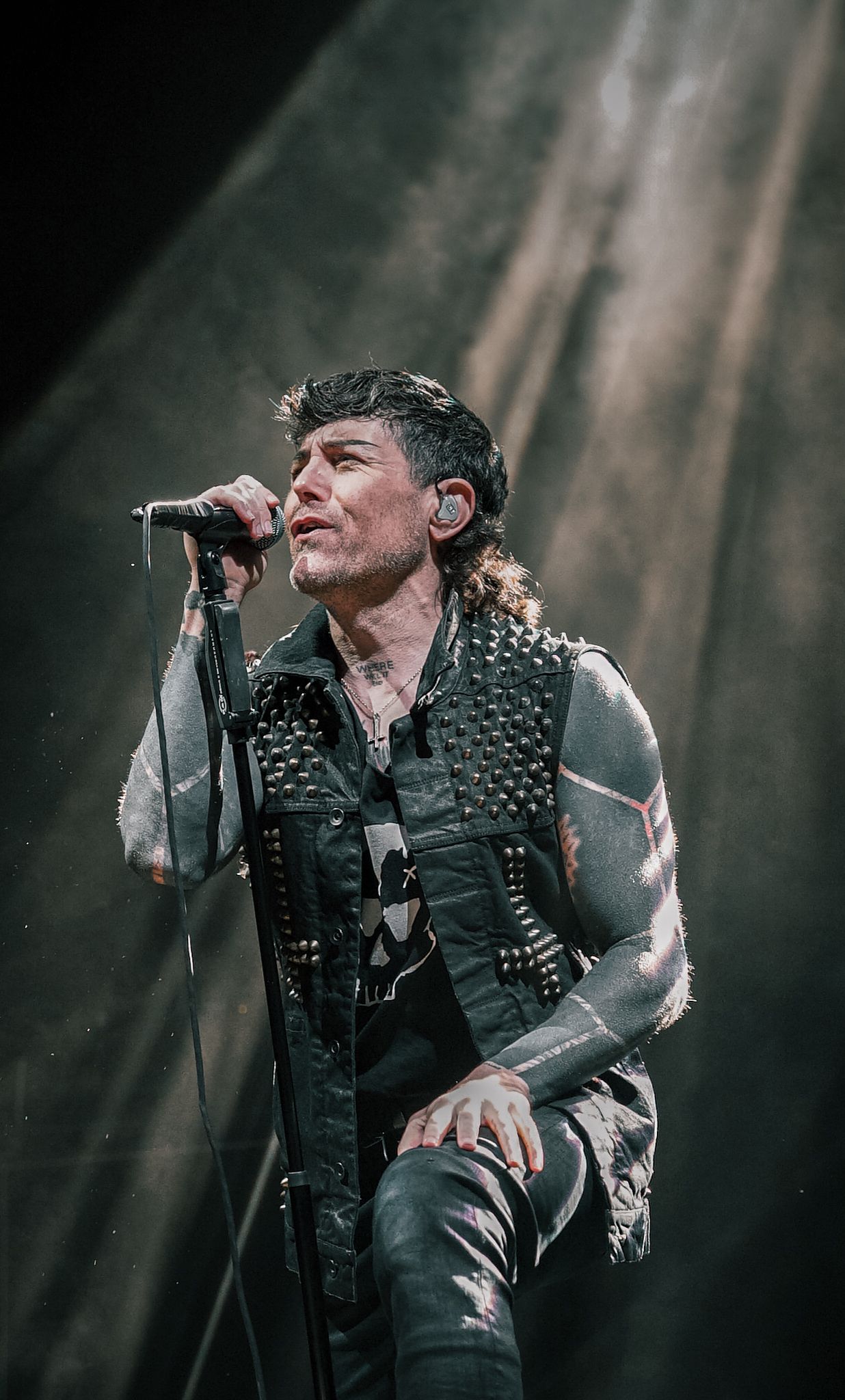 Rock performer in studded vest singing intensely during stage performance.