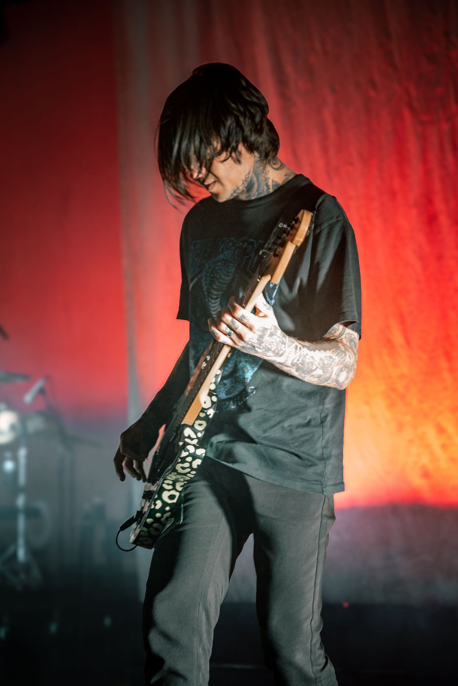 Rock performer plays guitar against red-lit backdrop during concert performance.
