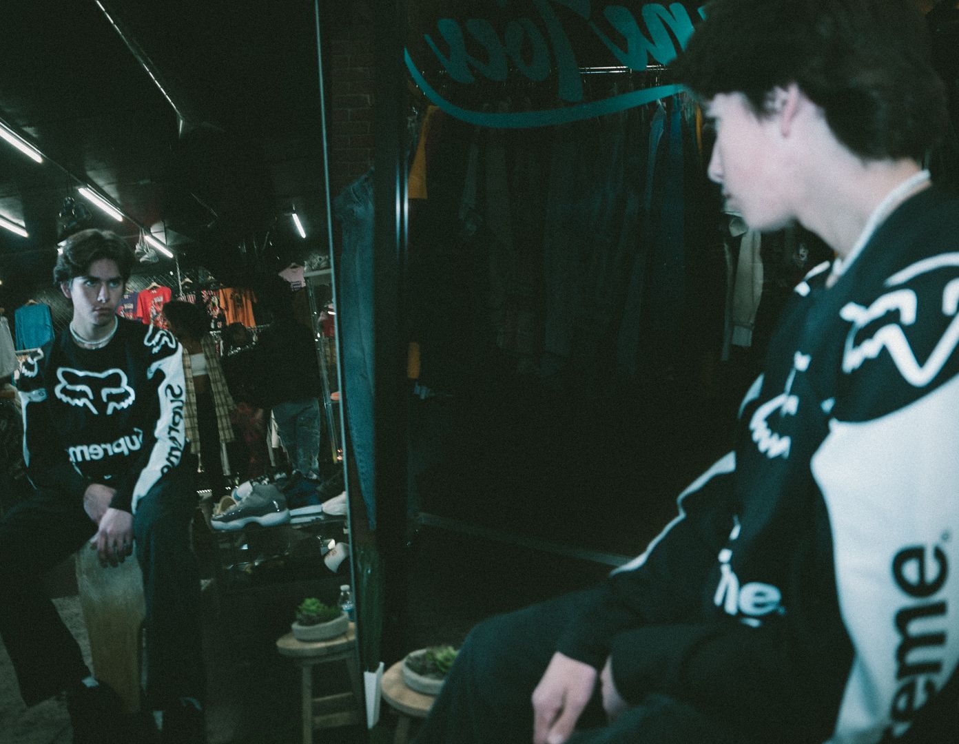 Dark indoor scene with Fox racing apparel and clothing racks visible.