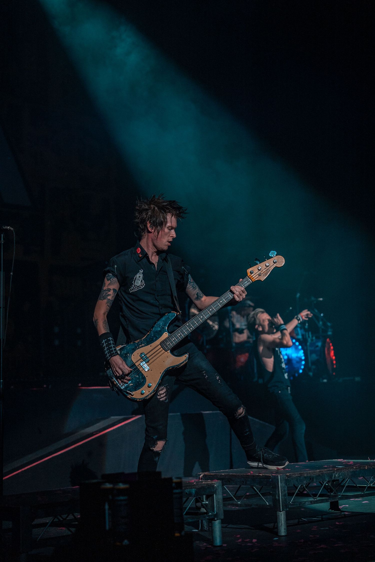 Bass guitarist performs energetically under blue stage lighting during rock concert performance.