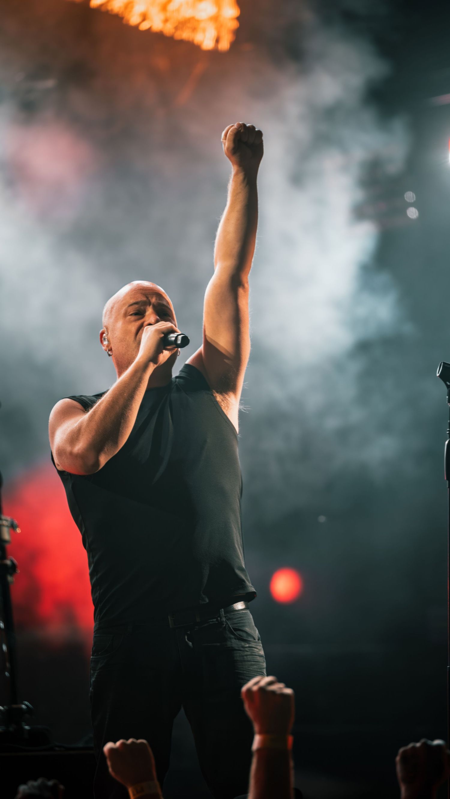 Singer performing energetically on stage with smoke effects and orange lighting in the background.
