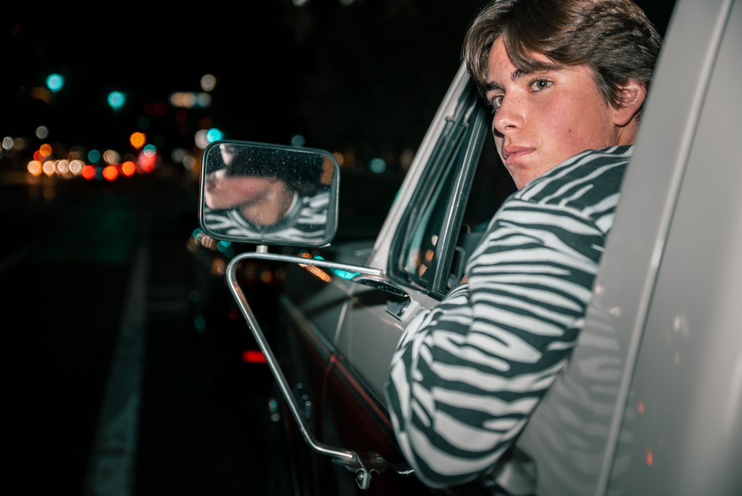 Side view portrait through car window with street lights in background.