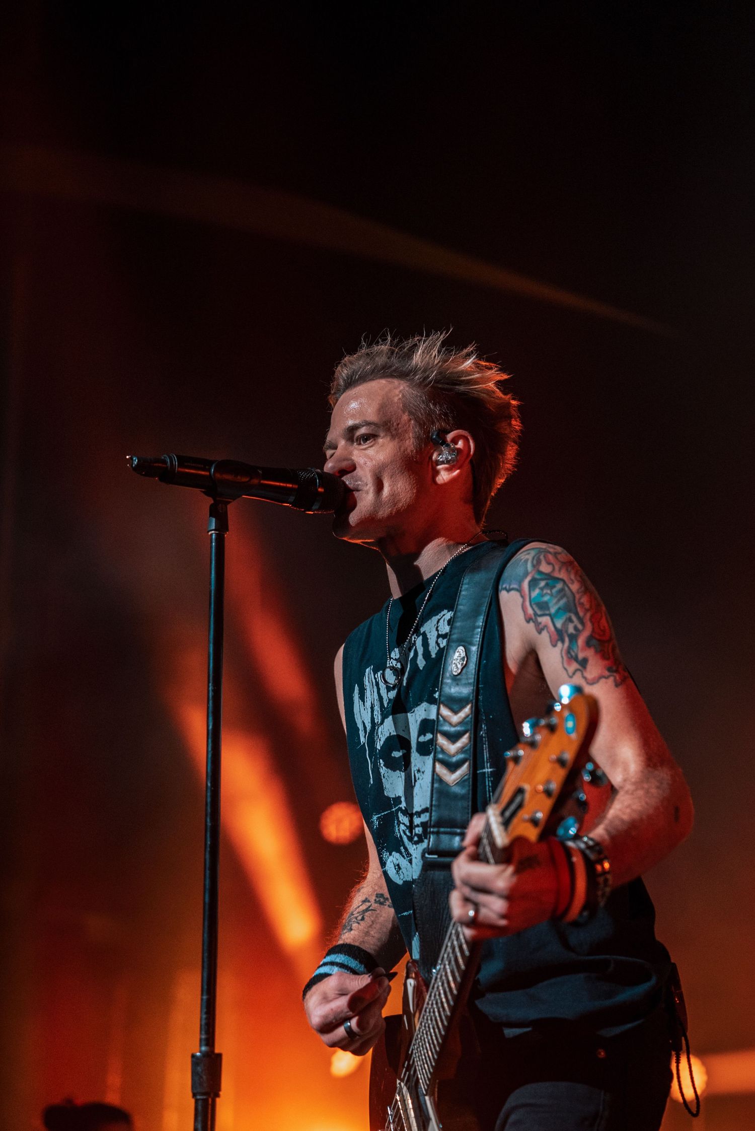 Musician playing guitar intensely against warm orange stage lighting.