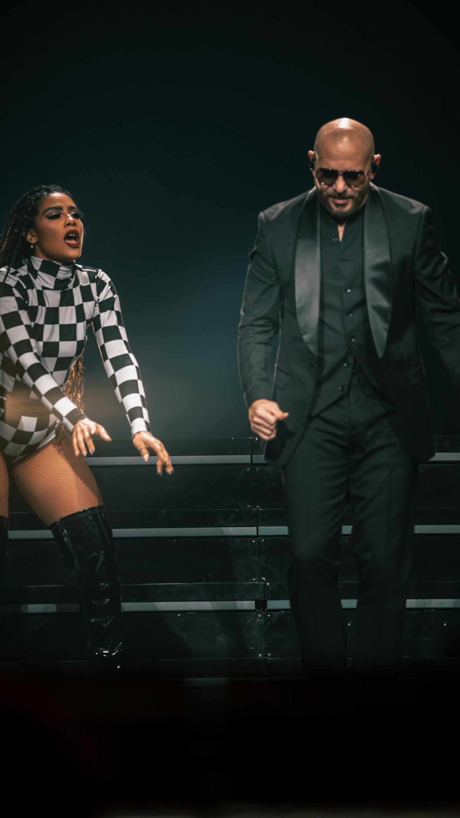 Performers in contrasting black suits and checkered costumes dance during dramatic stage show.