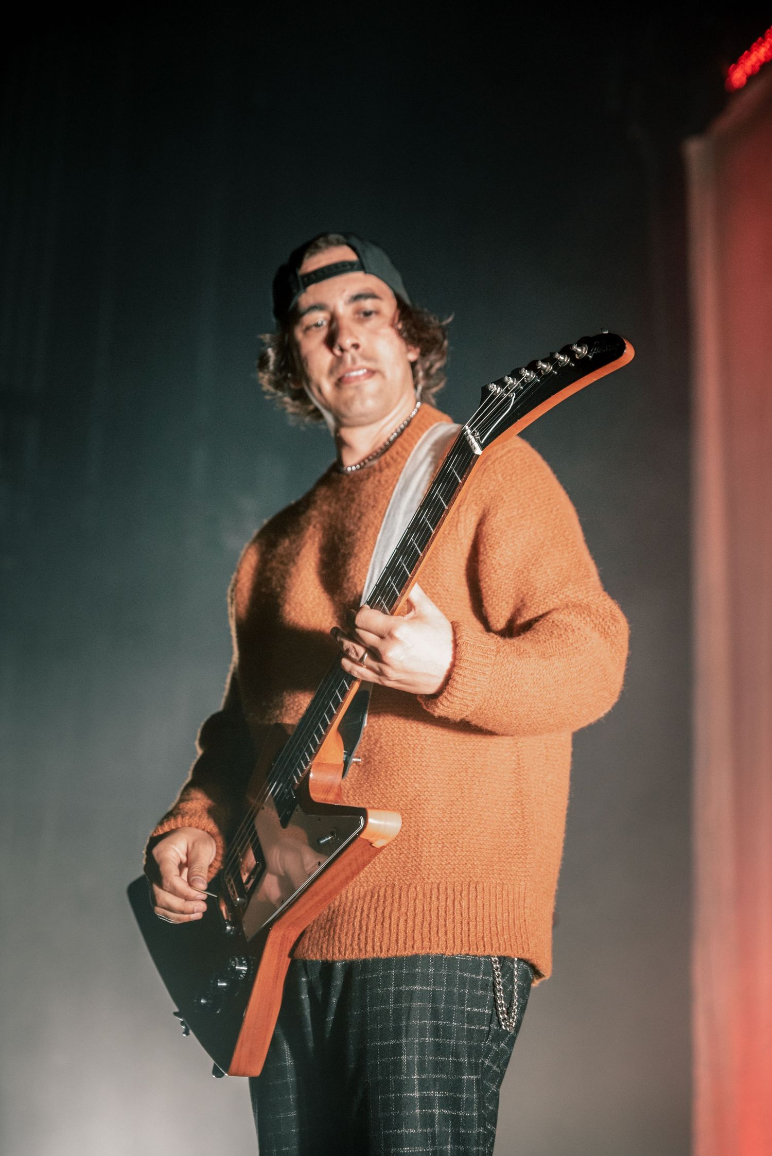 Musician in orange sweater playing guitar on stage during live performance.