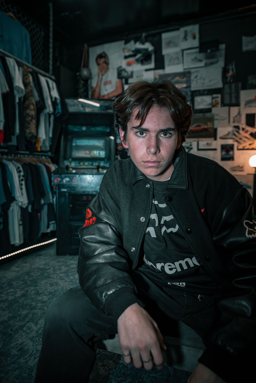 Moody portrait in clothing store with racks and posters in background.