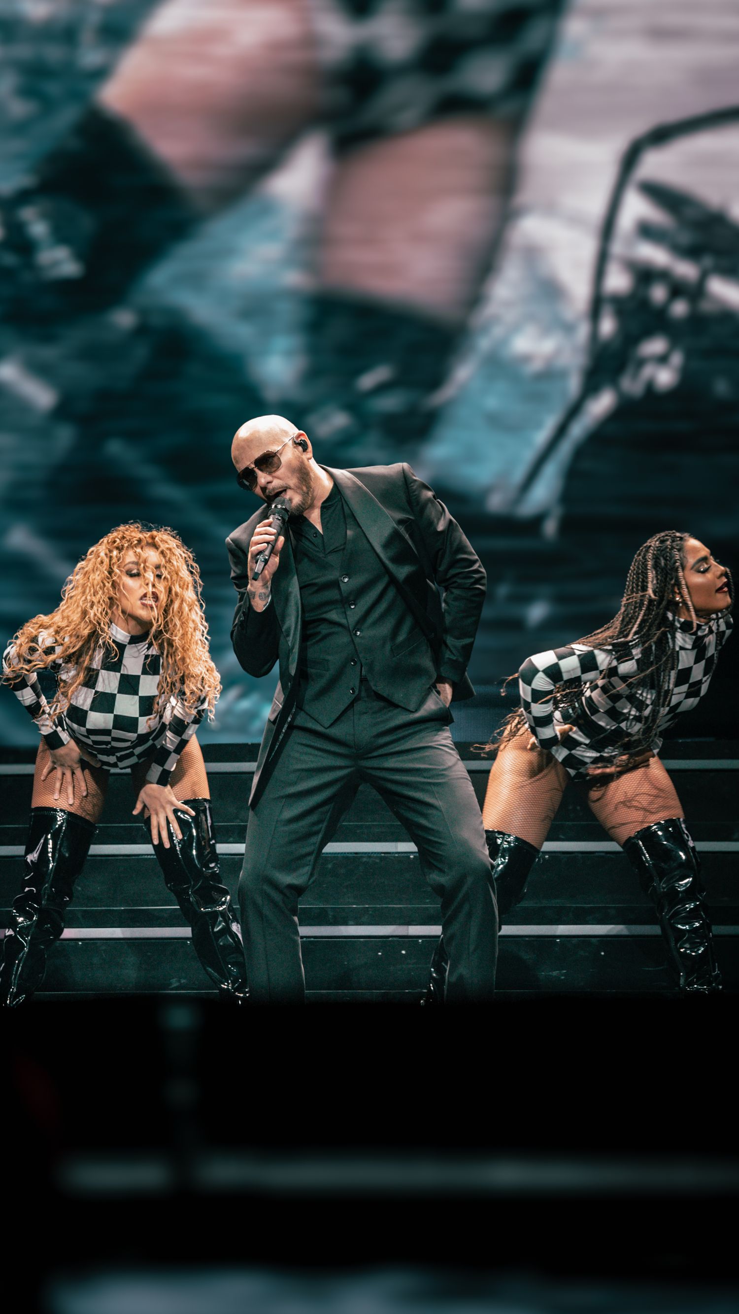 Dramatic dance routine with performers in black suits and checkered costumes on illuminated stage.