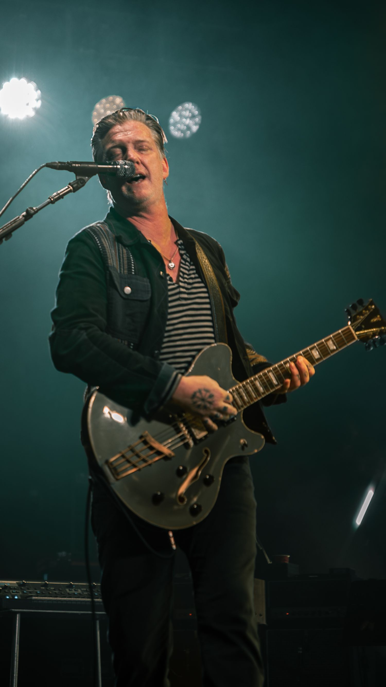 Musician plays silver electric guitar while performing under blue-green stage lighting.