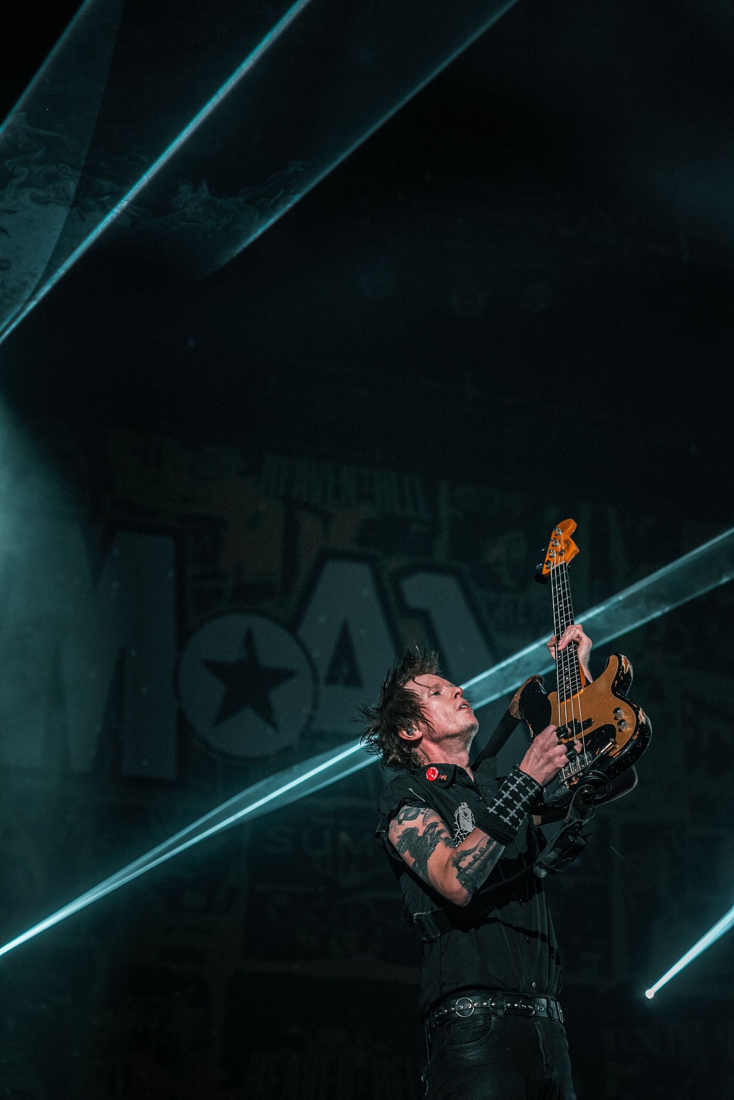Bassist performs under dramatic blue laser beams on dark concert stage.