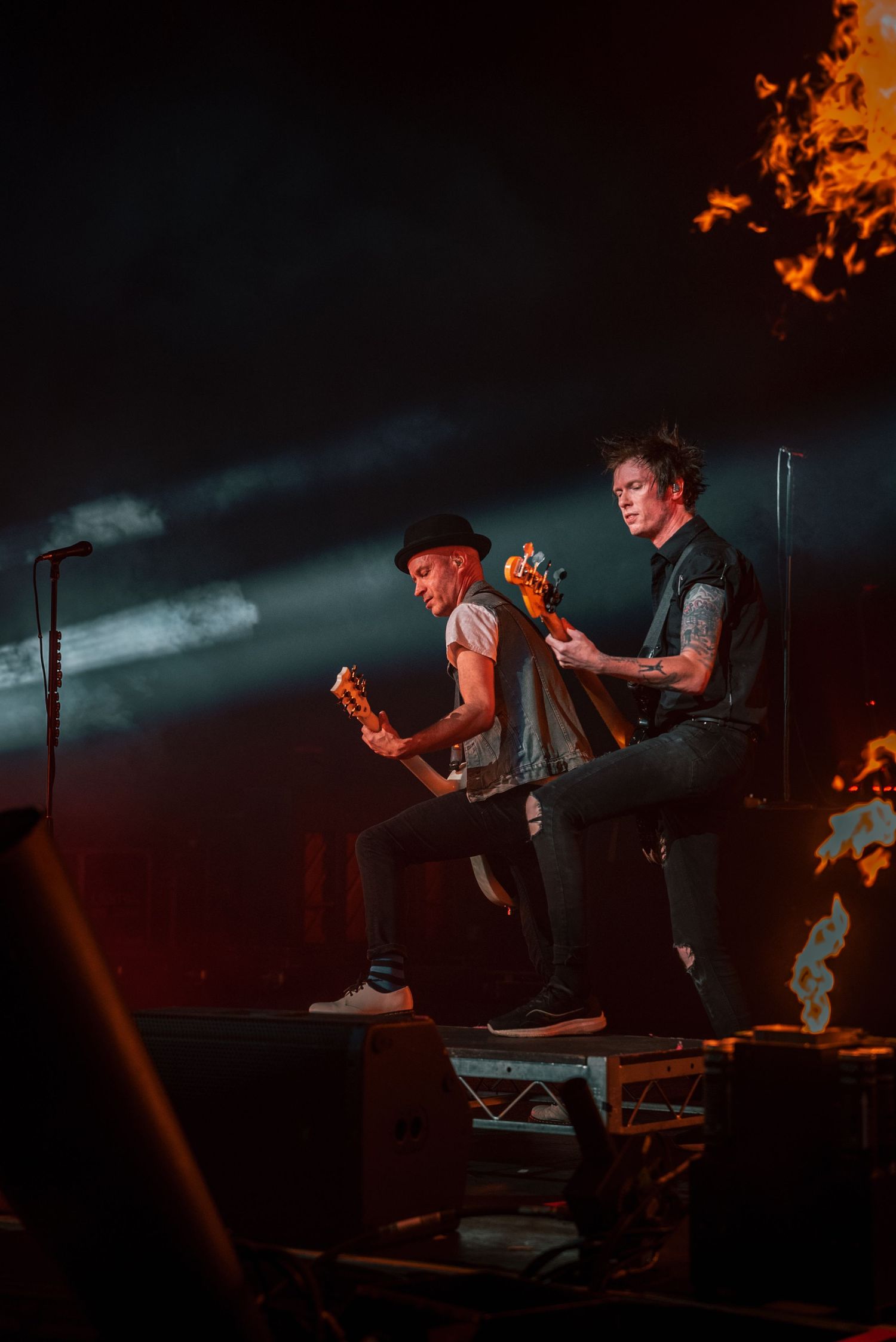 Musicians rock out on elevated platform with dramatic fire effects and moody lighting.