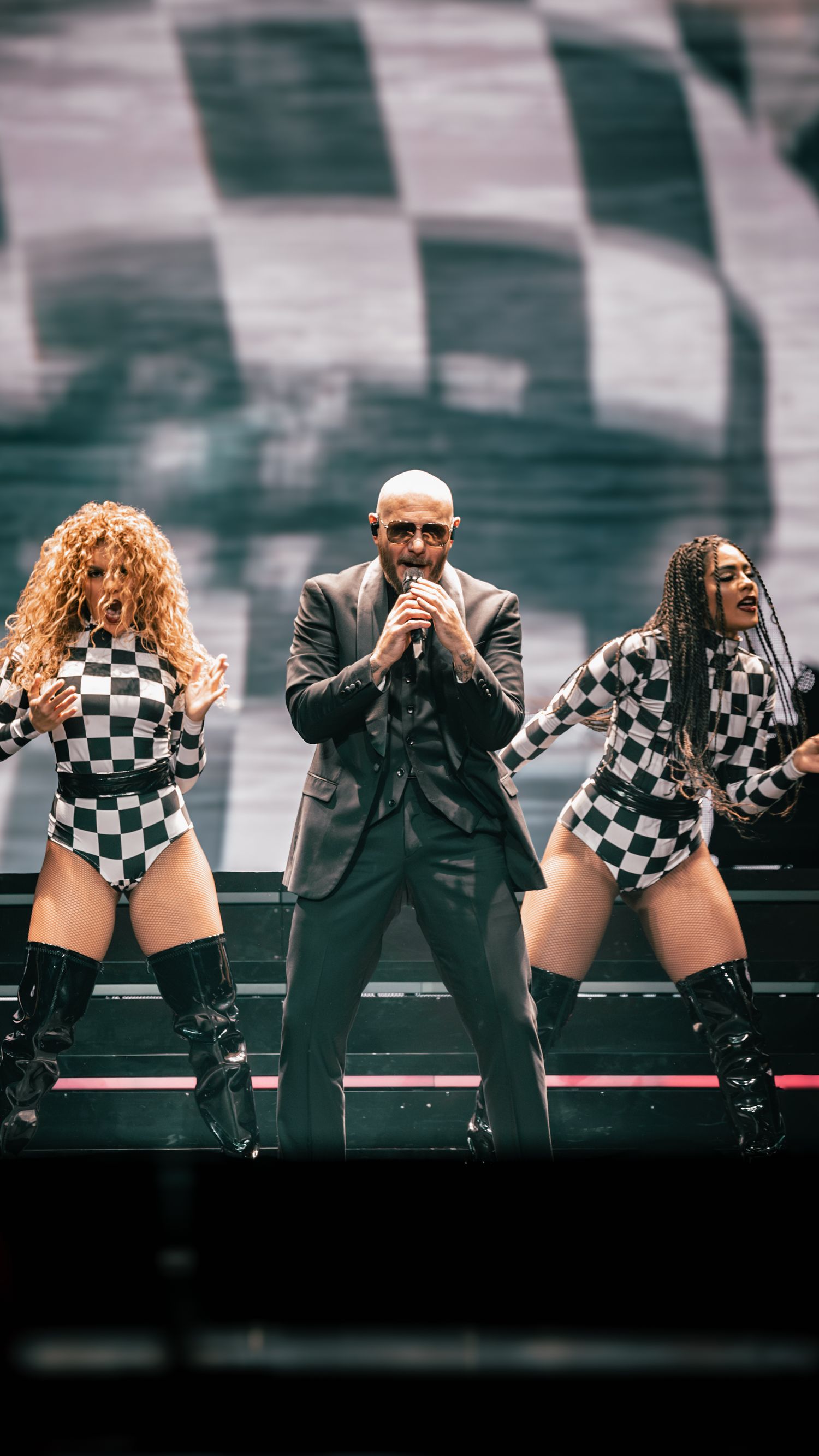 Performers execute synchronized dance moves in matching checkered outfits and dark suits.