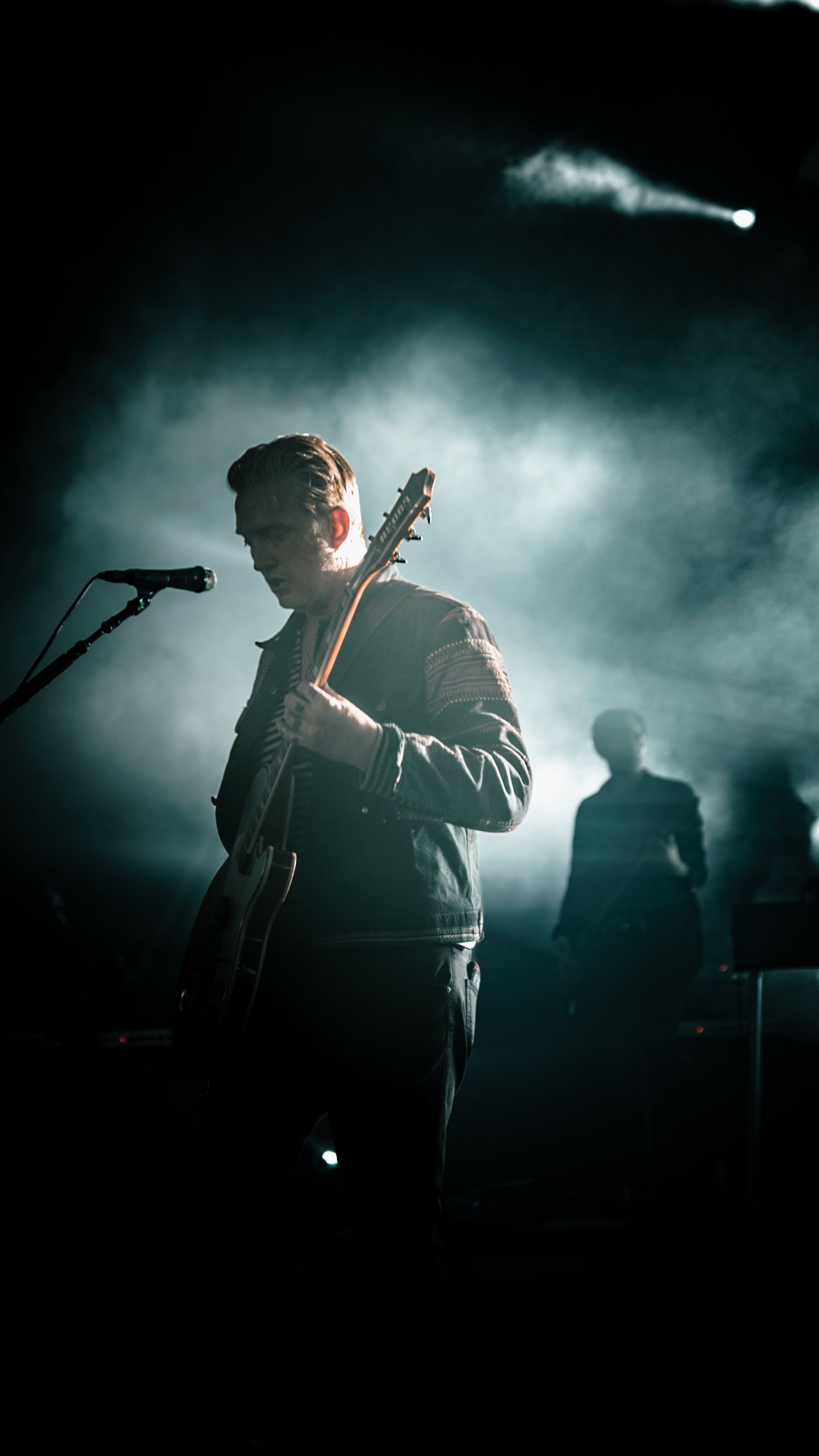 Dramatic silhouettes of performers on stage backlit by moody blue lighting and atmospheric fog effects.