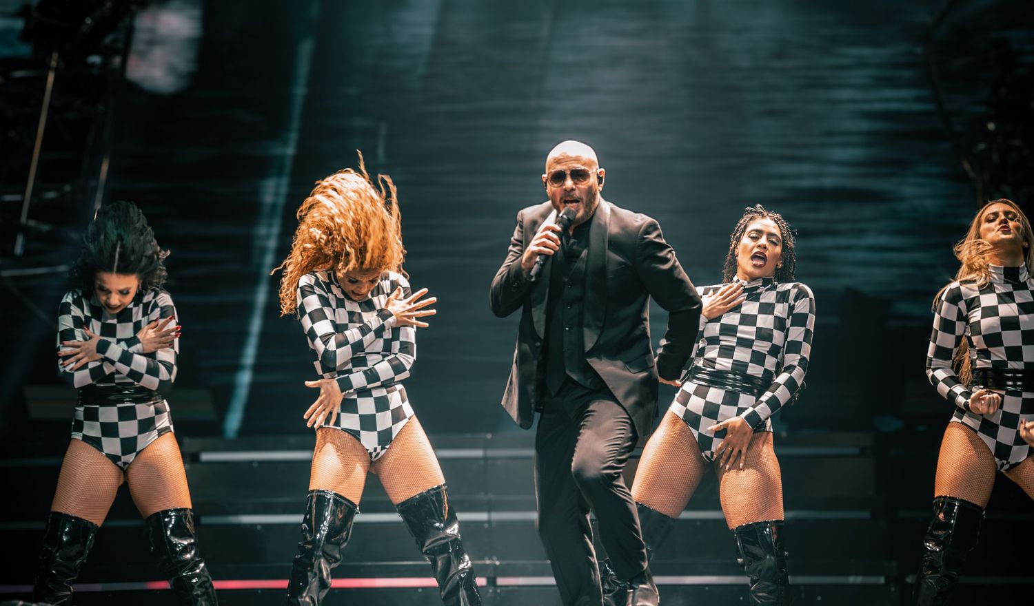 Dancers in checkered outfits performing choreographed moves on stage during a show.