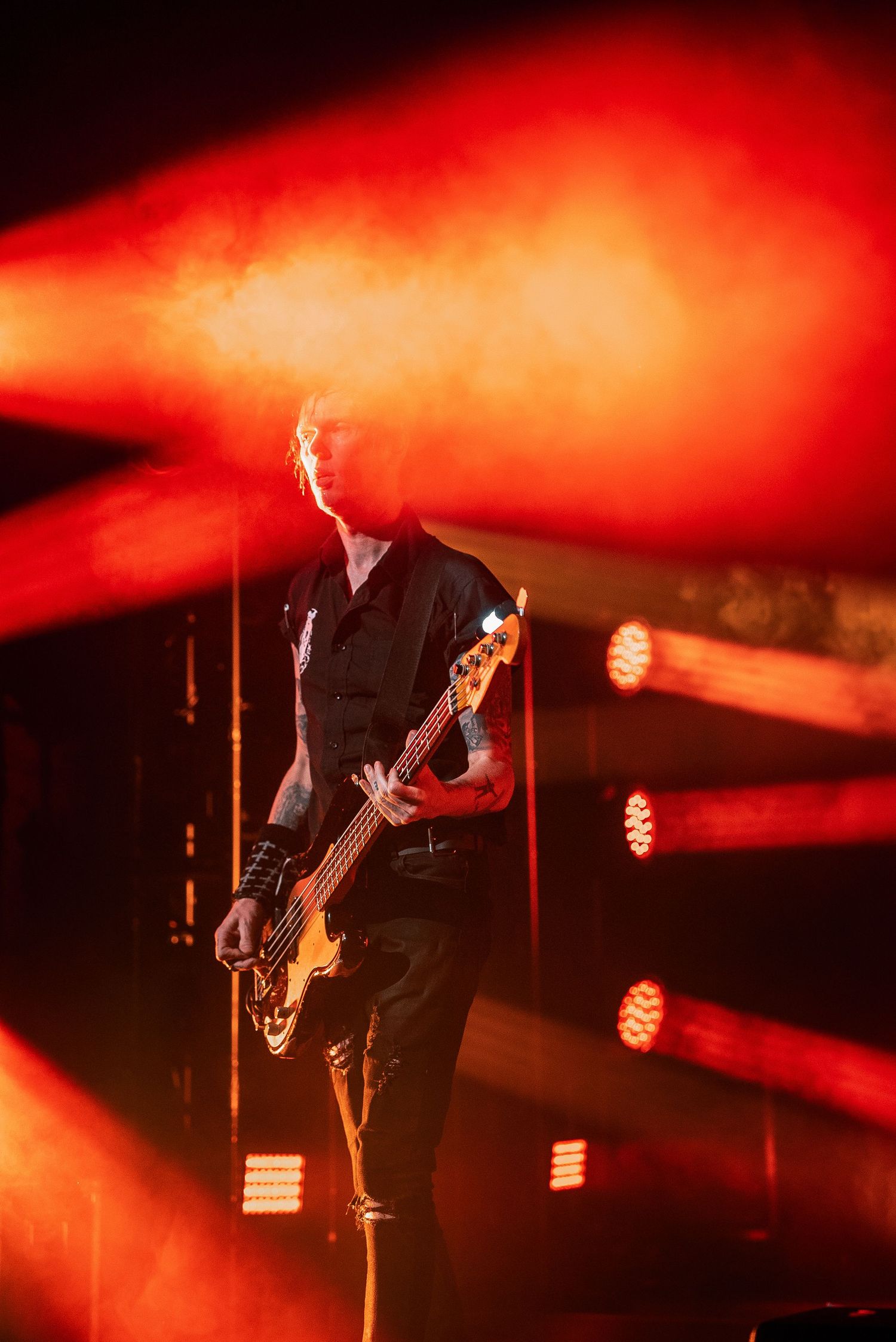 Bassist silhouetted against dramatic red stage lighting during rock performance.