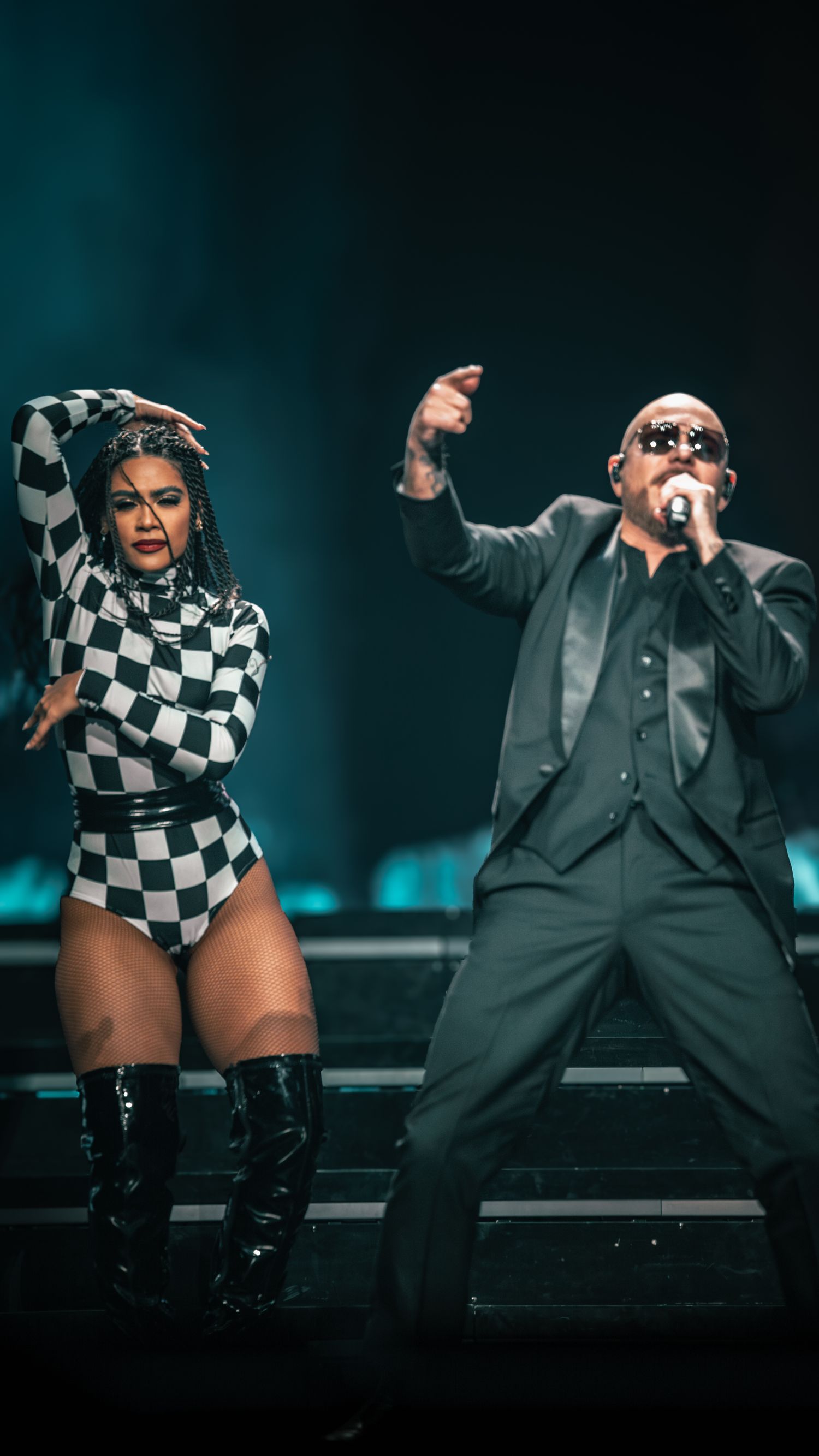 Dramatic concert scene with performers in coordinated black and white costumes against teal backdrop.