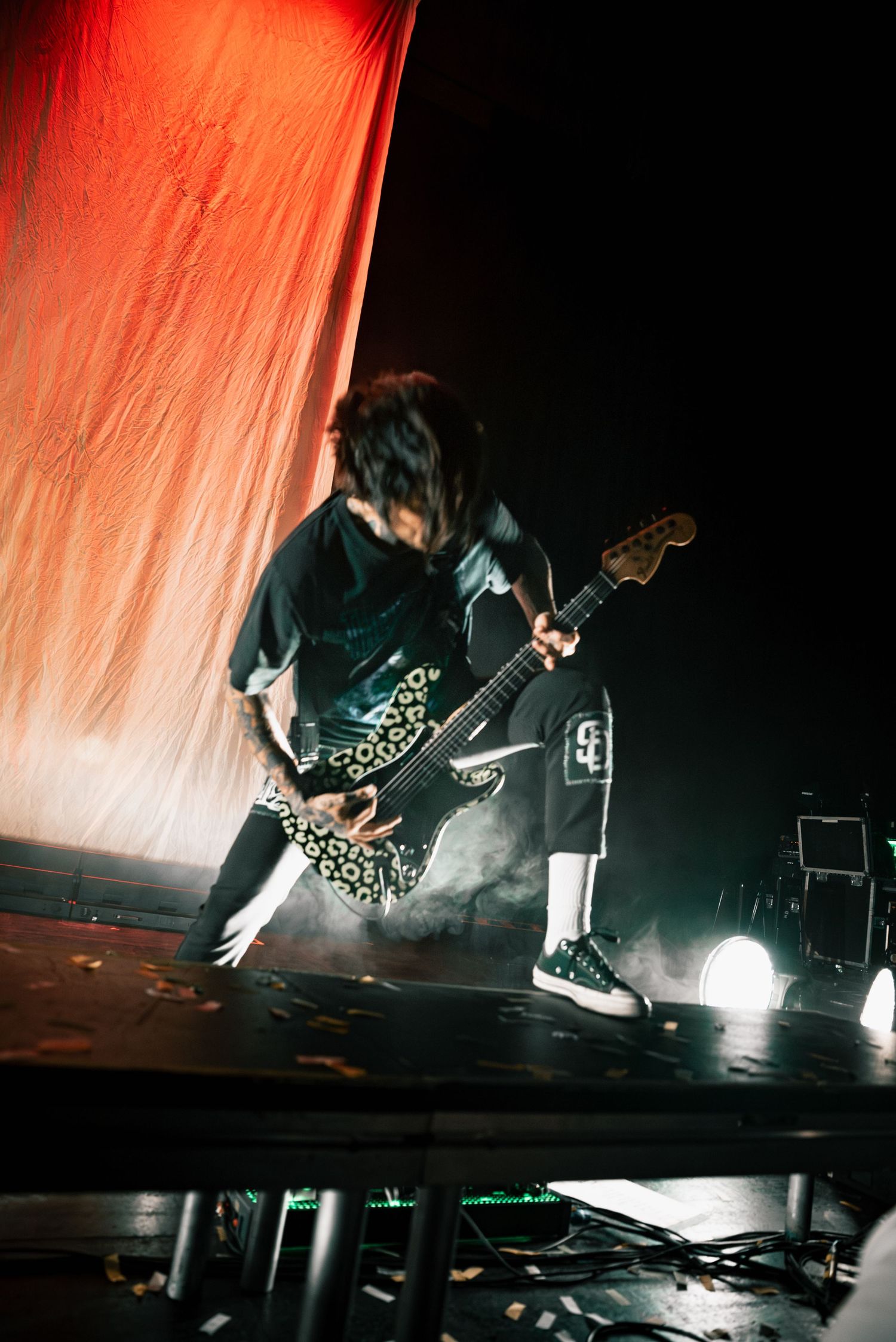 Dynamic stage performance with guitarist silhouetted against dramatic orange lighting.