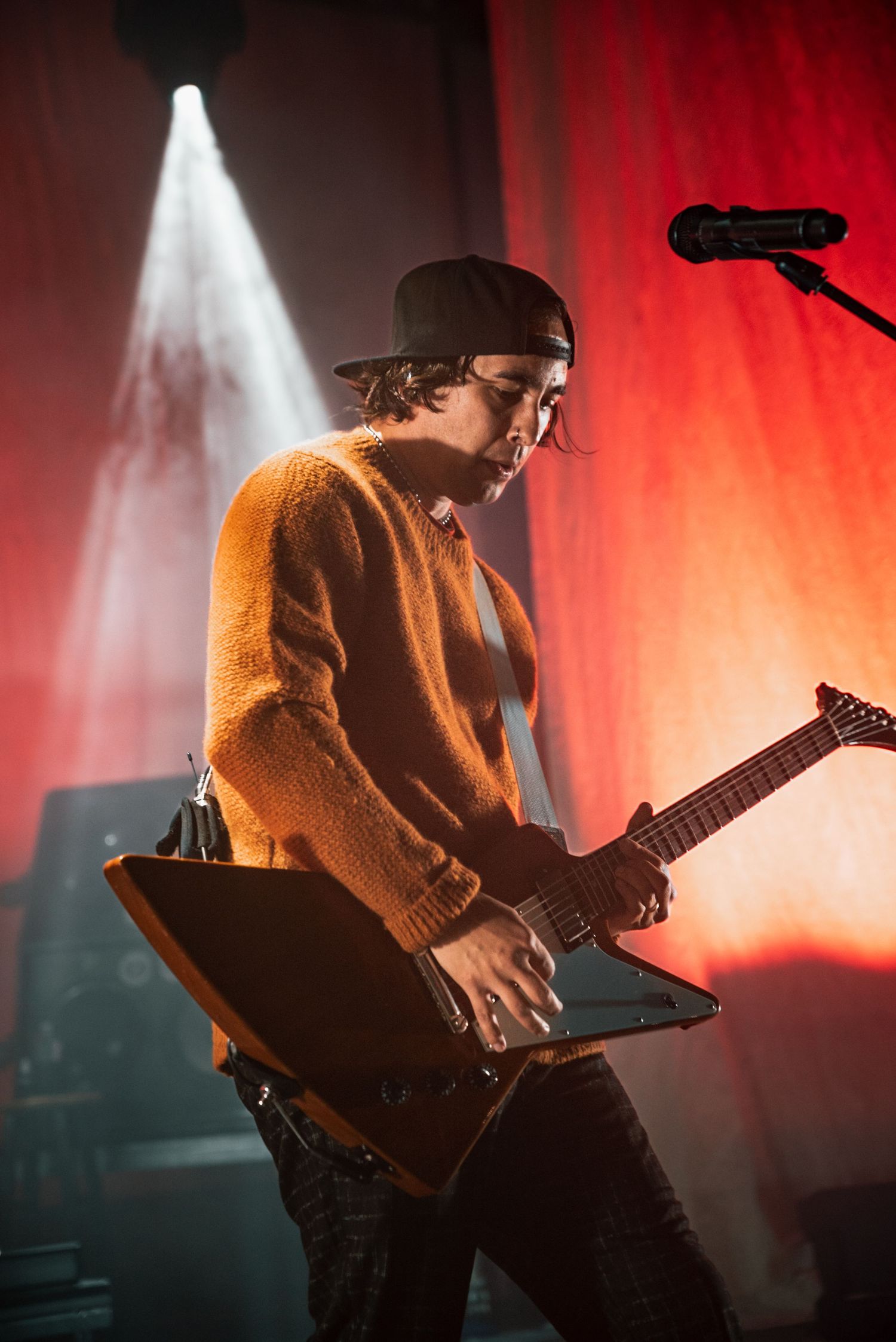 Guitarist in casual attire plays modern electric guitar under dramatic stage lighting and fog effects.