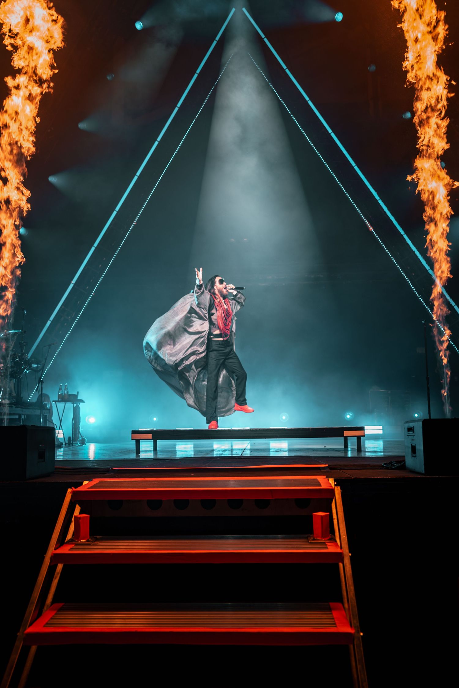 A dramatic stage performance with fire effects and a blue triangle backdrop.