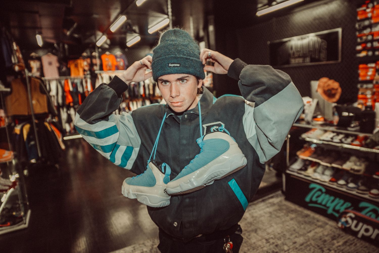A street fashion scene showing someone posing with a turquoise and gray sneaker in a shoe store.