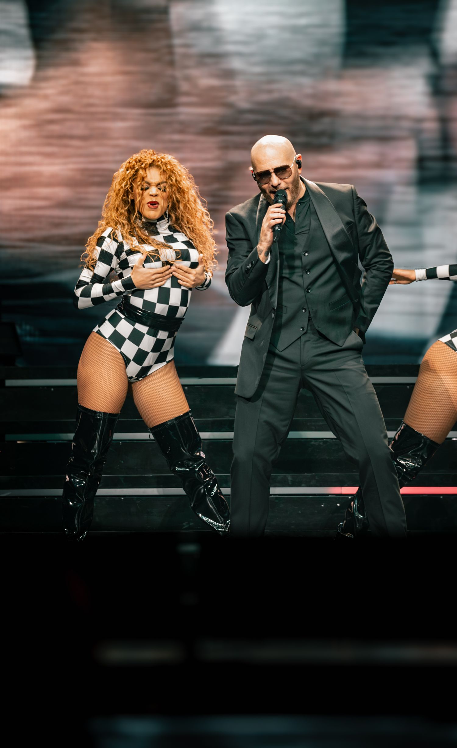 Dynamic stage choreography featuring performers in contrasting formal and checkered costumes.