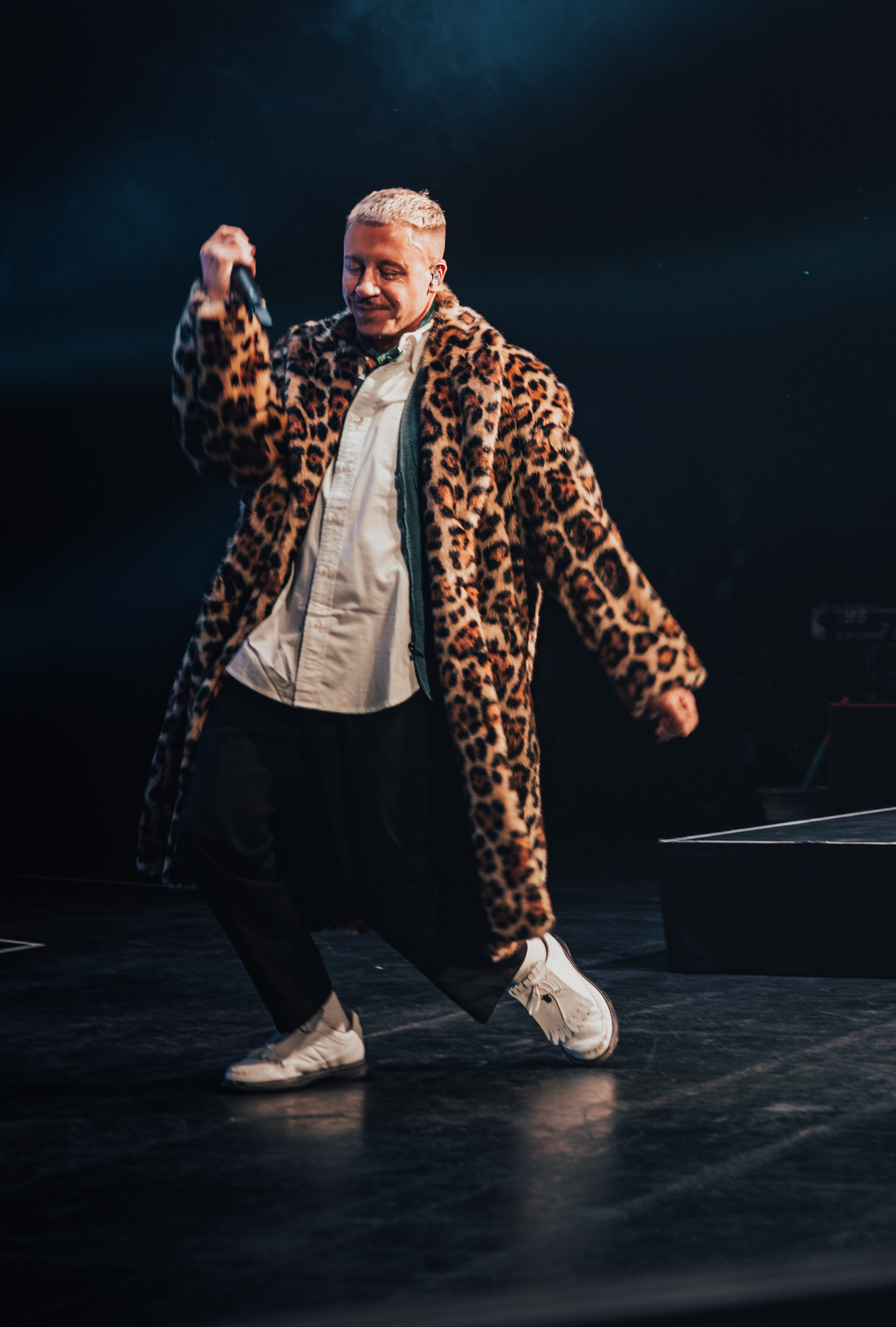 Dramatic low-angle shot of a performer in leopard print coat crouching on stage during a show.