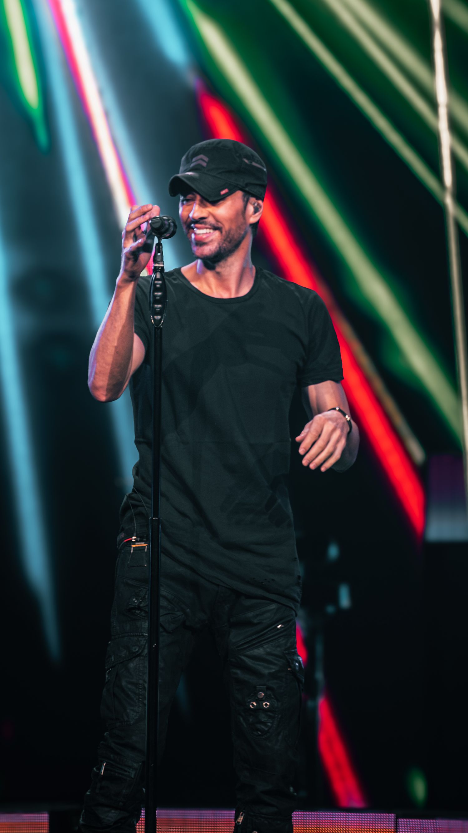 Singer in black outfit performing on stage with colorful laser light effects in background.