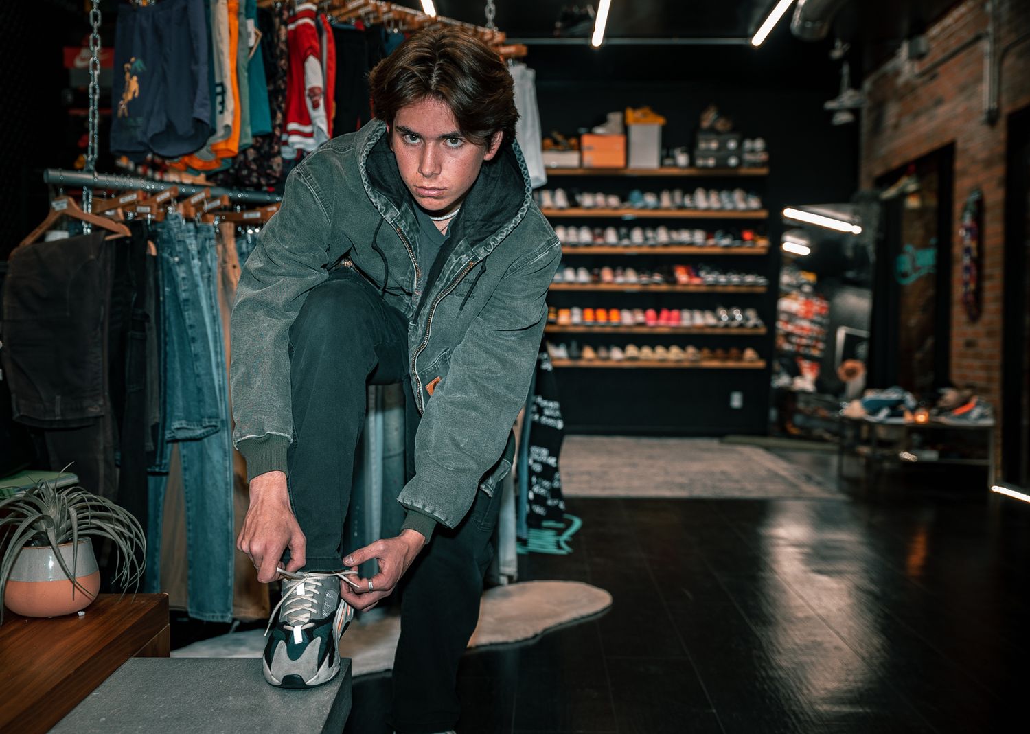 Person in green jacket bending down to tie shoes in dimly lit retail space.