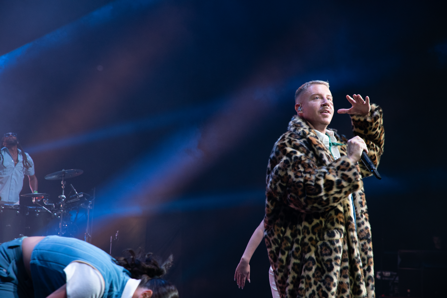 Performer in a leopard print coat dancing energetically on a dimly lit stage.