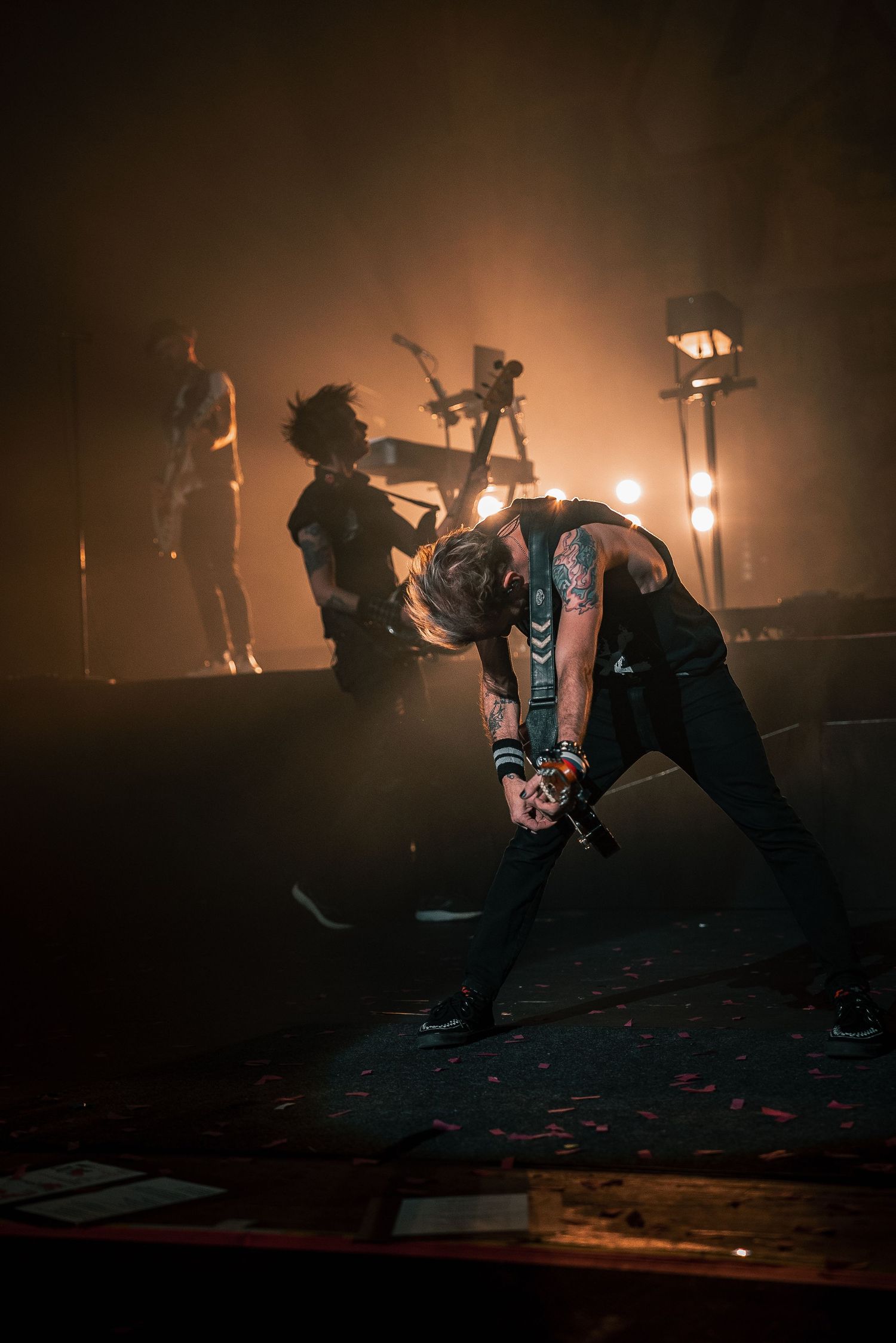 Band members performing energetically on dimly lit stage with warm ambient lighting.