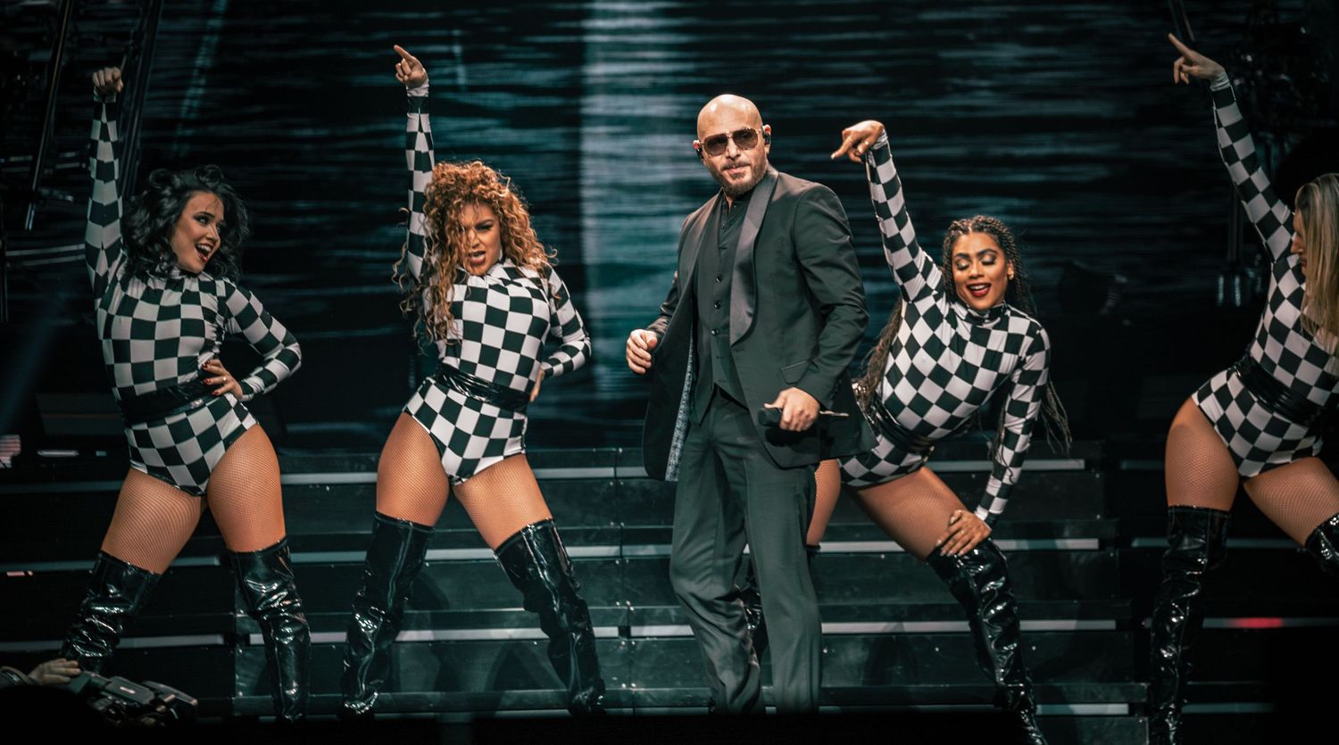 Dynamic stage performance featuring dancers in checkered outfits and performer in green suit.